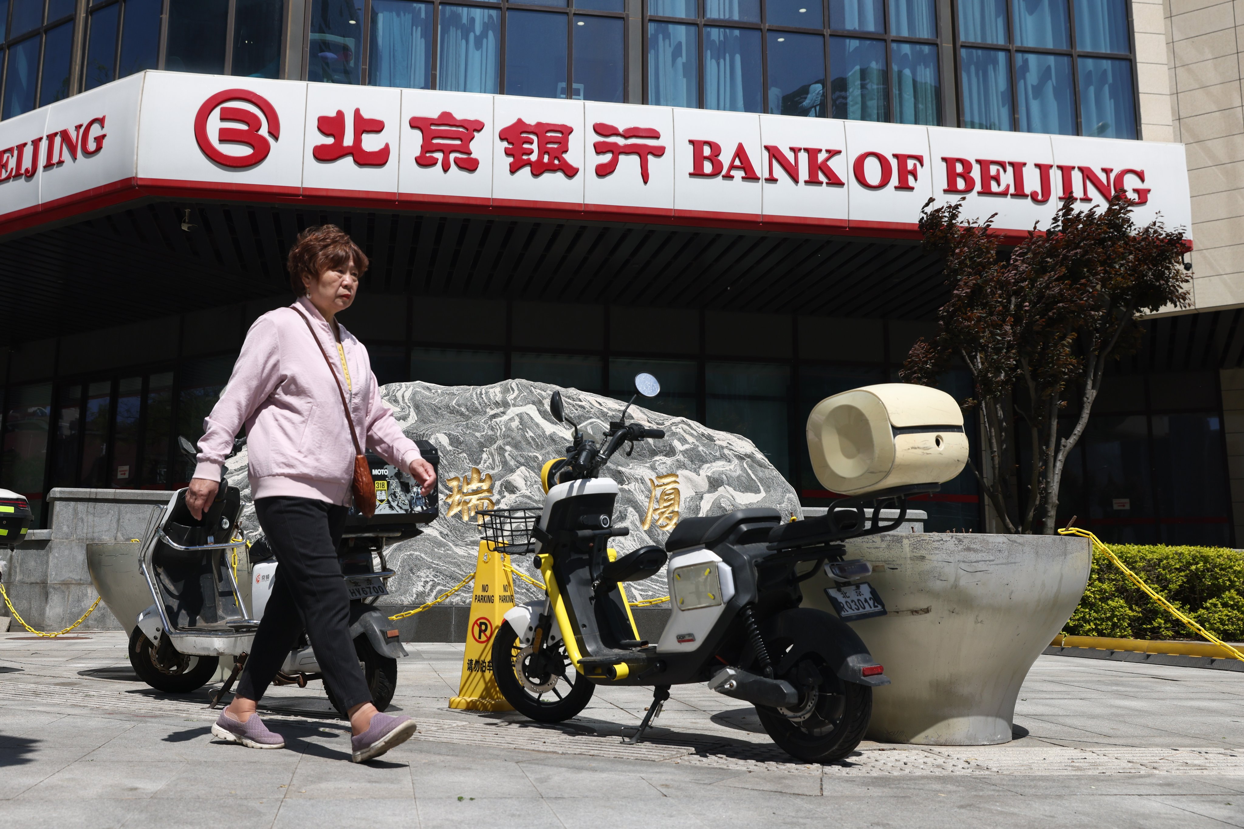 An elderly woman walks past a bank branch in Beijing on April 20. Photo: EPA