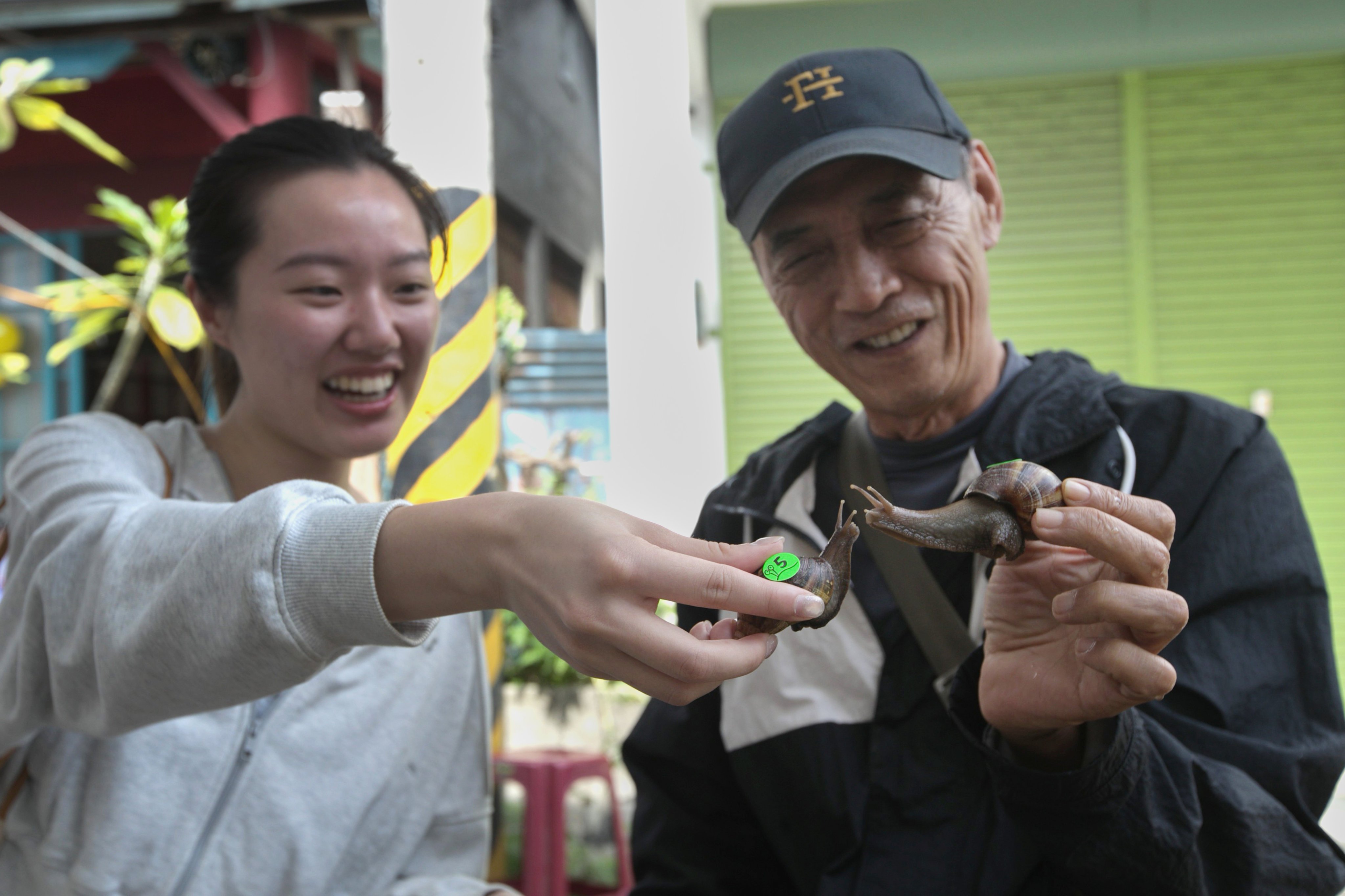 Alysa Chang, left, and Li Cheng-wen hold up their snail racers in Fenglin town, Hualien County, eastern of Taiwan, Saturday, May 2, 2026. (AP Photo/Chiang Ying-ying)