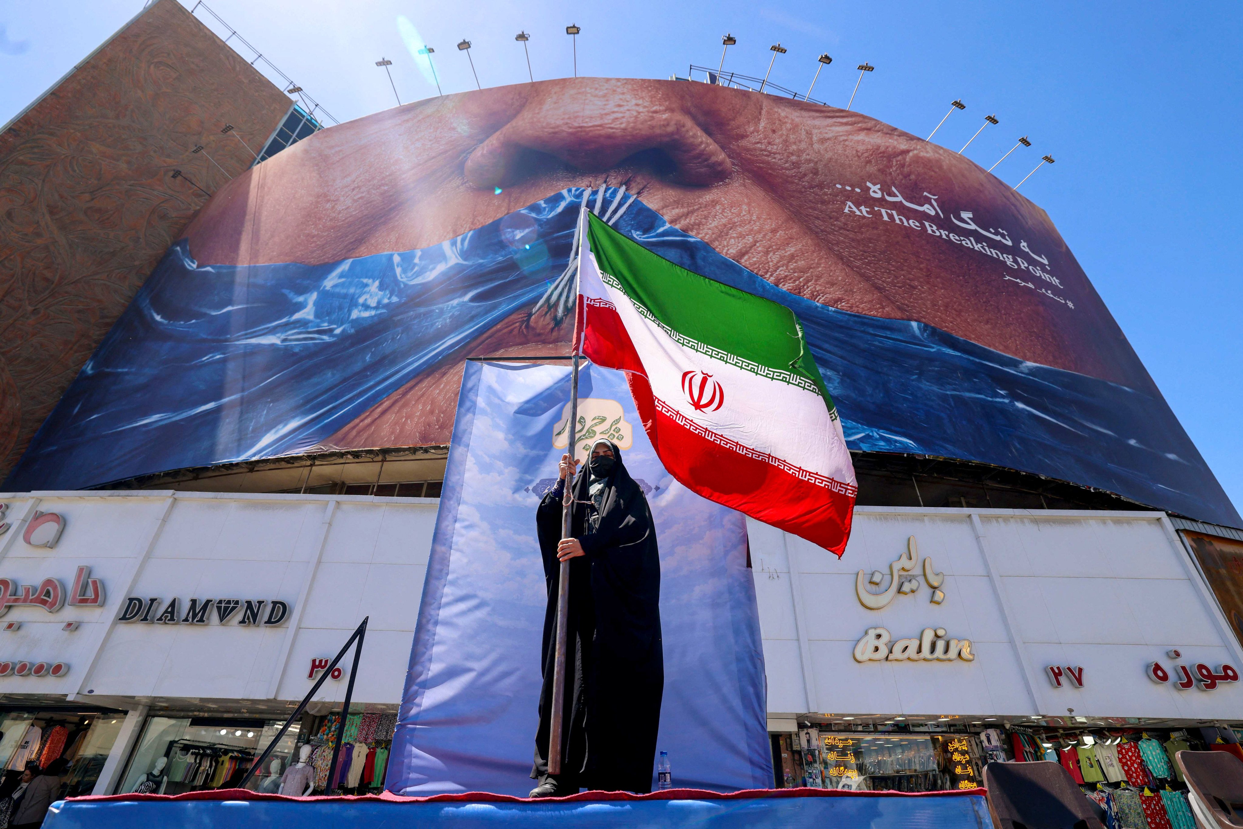 A woman holds the Iranian flag as she stands in front of an anti-US billboard in Tehran on Sunday. As the war enters its tenth week, peace talks remain stalled. Photo: AFP