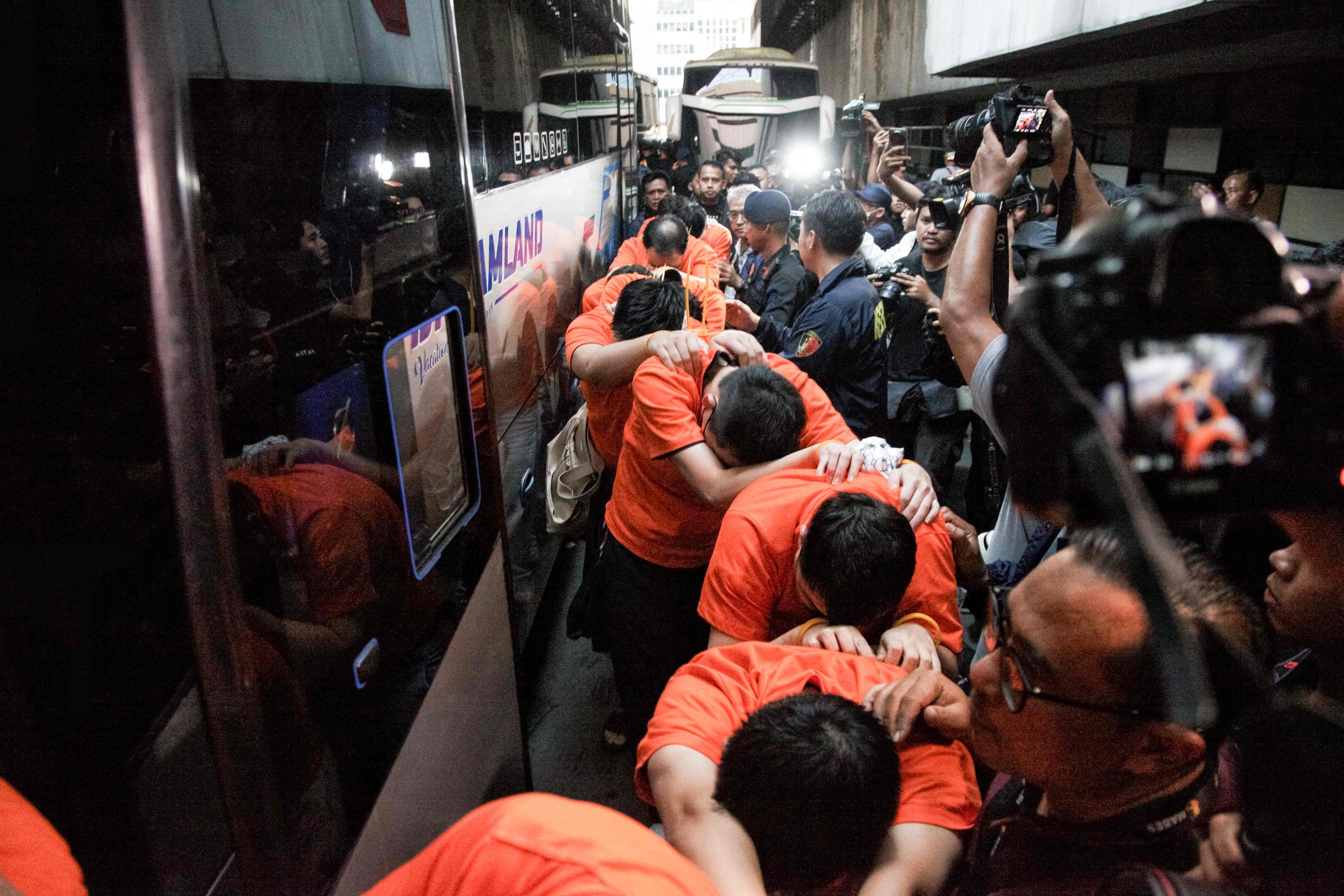 Suspected online gambling operators (in orange) walk towards buses for transfer after a police raid at the Hayam Wuruk Plaza office building in Jakarta on May 10, 2026. Indonesian police and immigration authorities said they arrested 321 foreign nationals, including suspects from Vietnam, China, Myanmar, Laos, Thailand, Malaysia and Cambodia. (Photo by Aditya Irawan / AFP)