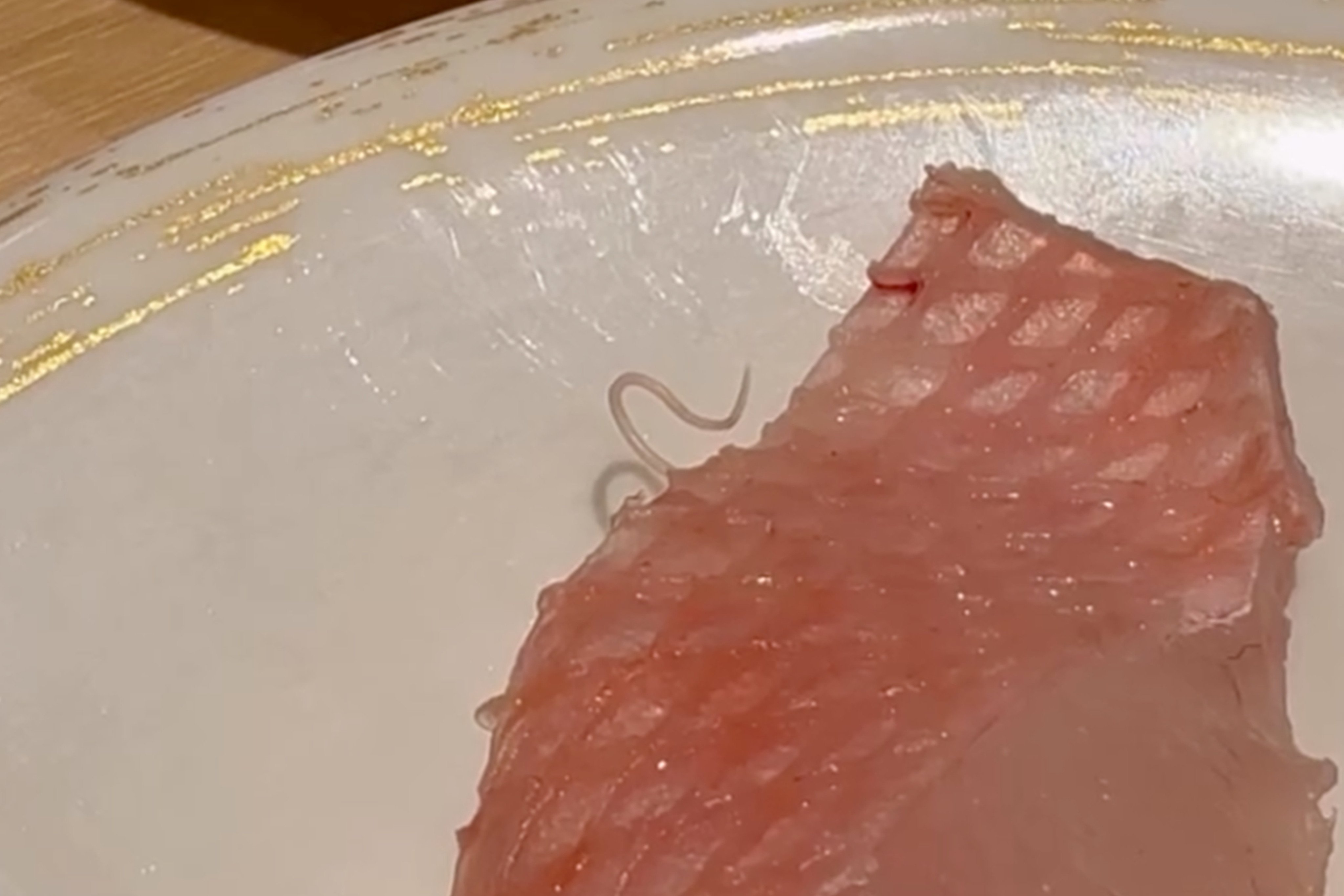 A sushi restaurant has apologised after a customer spotted a thread-like parasite crawling out of a piece of sashimi. Photo: Threads/aworminmysushi