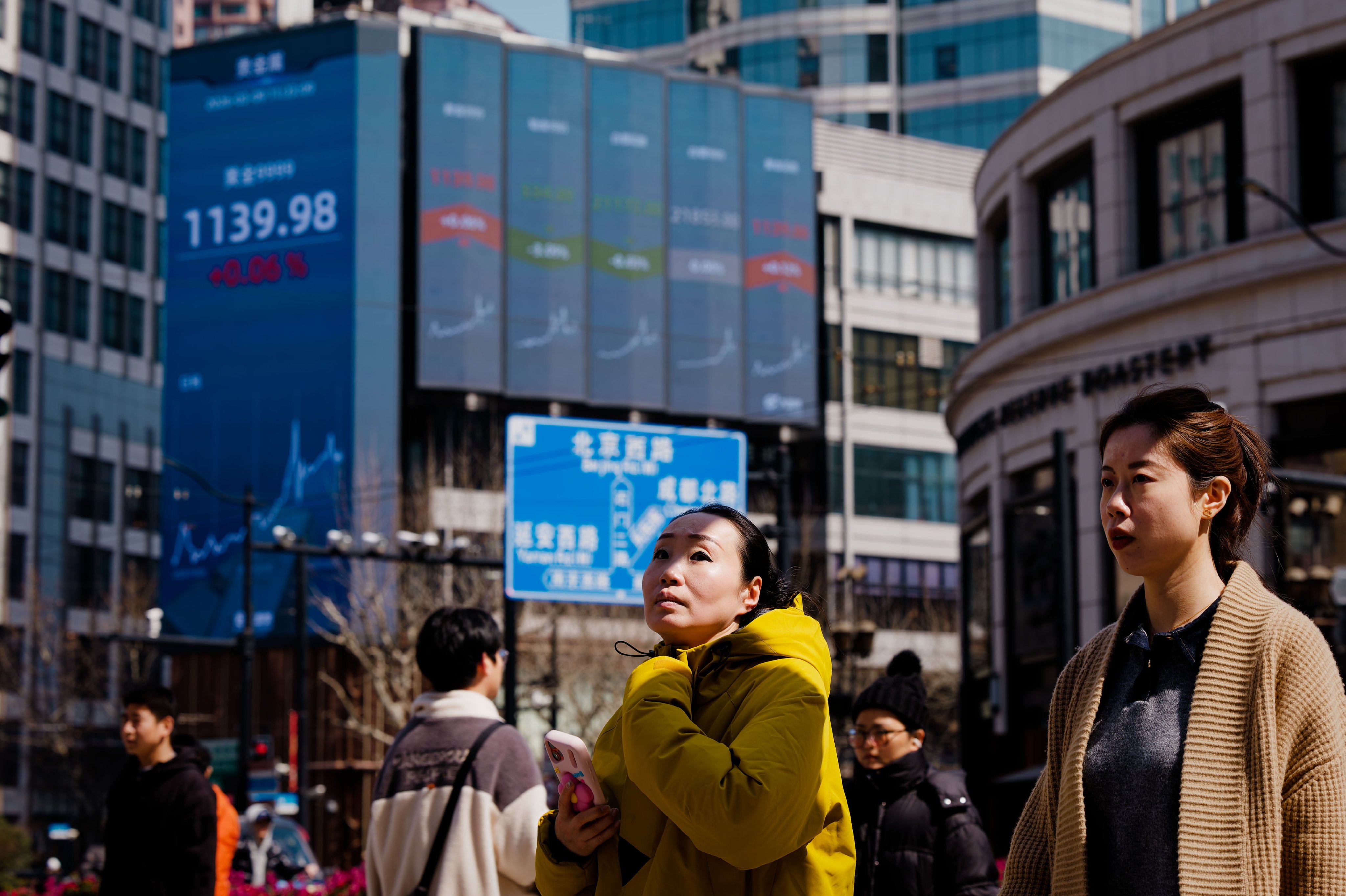 People cross the street beneath a large screen showing the latest stock exchange data in Shanghai. Photo: EPA