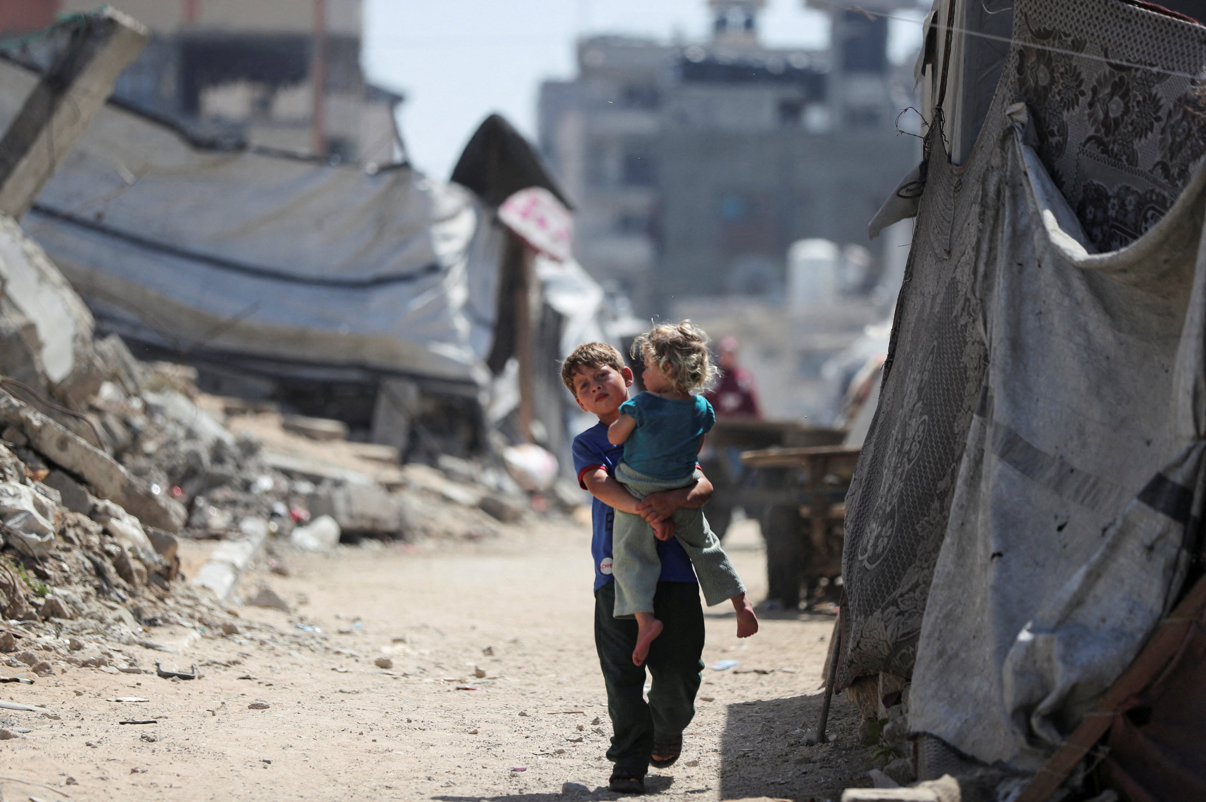A Palestinian boy, carrying a girl, walks through a damaged area amid the rubble of residential buildings in Gaza City on Monday. Photo: Reuters