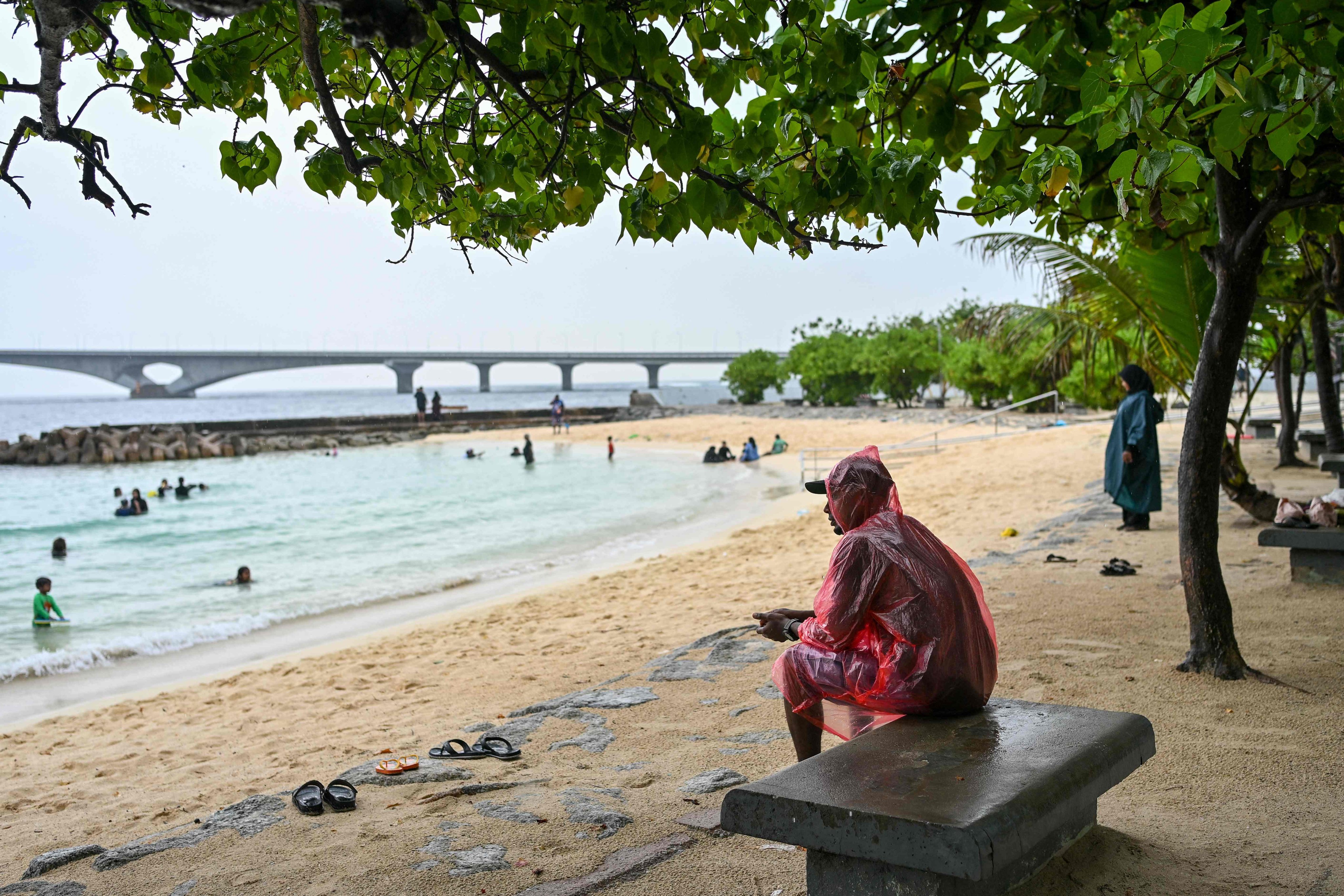 A man sits under a tree during rain in Malé in the Maldives on Friday, as rescue teams continued to search for the bodies of a group of Italians who died while diving. Photo: AFP