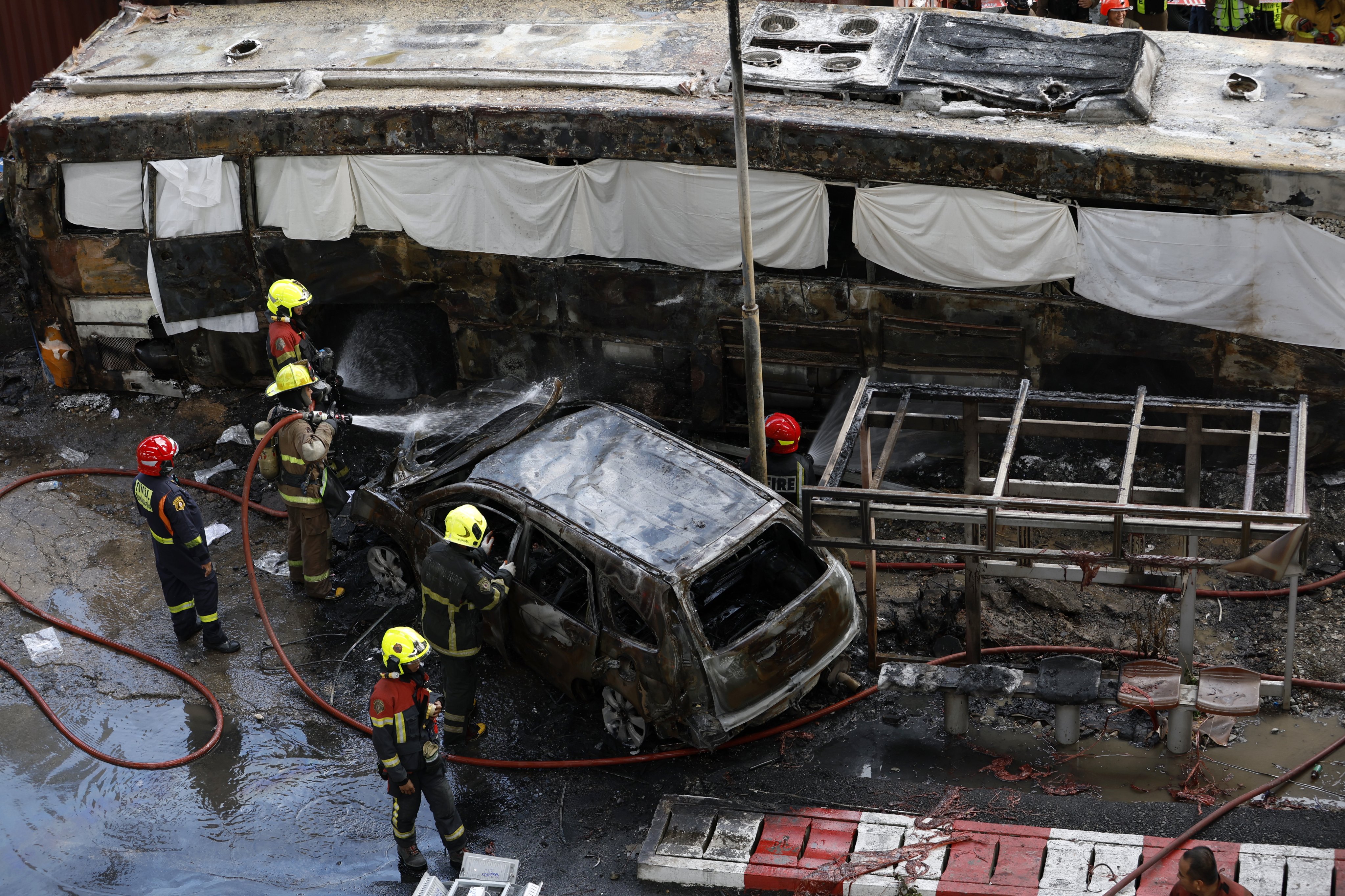 Rescuers extinguish a damaged car and a wrecked public bus that burst into flames following Saturday’s goods train crash in Bangkok, Thailand. Photo: EPA