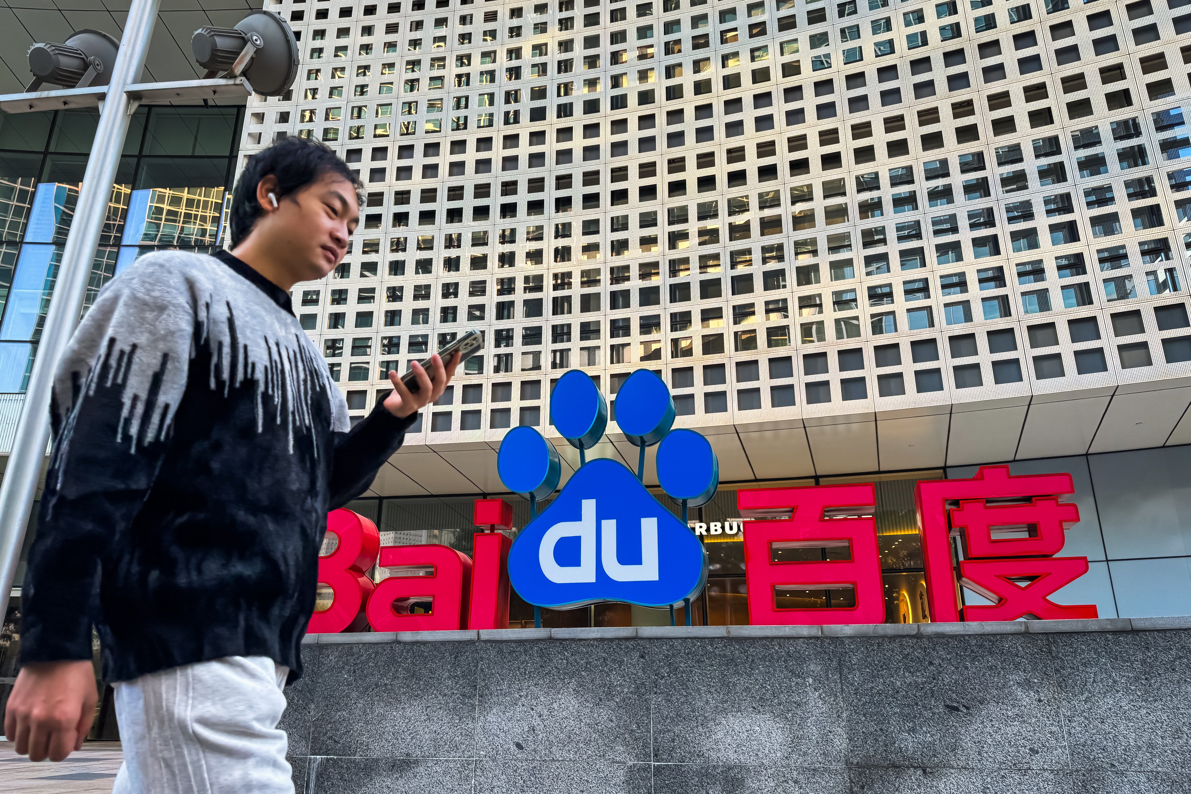 The Baidu building in Shenzhen displays the company’s logo as a pedestrian using a smartphone walks by. Photo: Getty Images