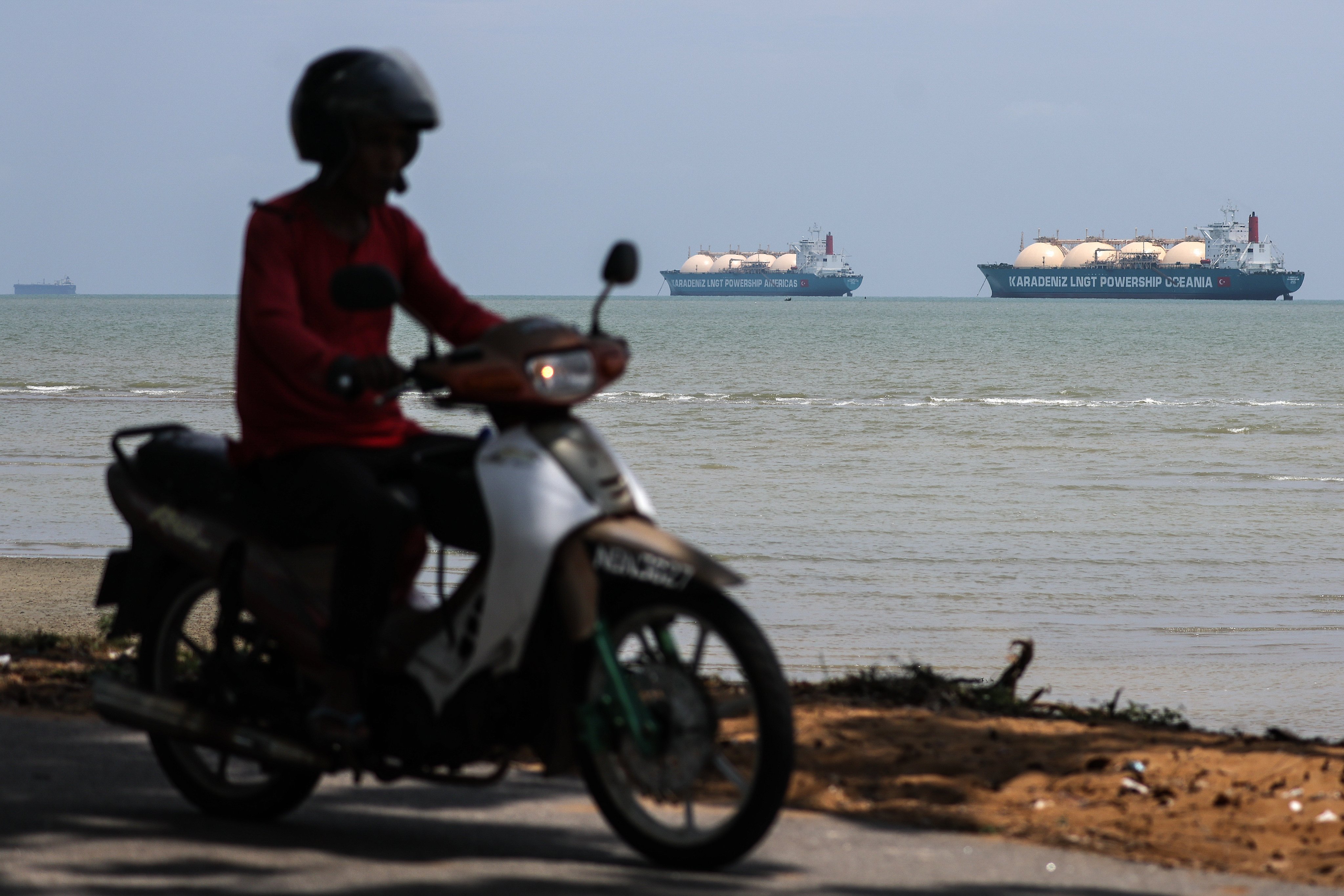 A motorcyclist passes by liquefied natural gas tankers in the Malacca Strait off the coast of Malaysia on April 15. Photo: EPA