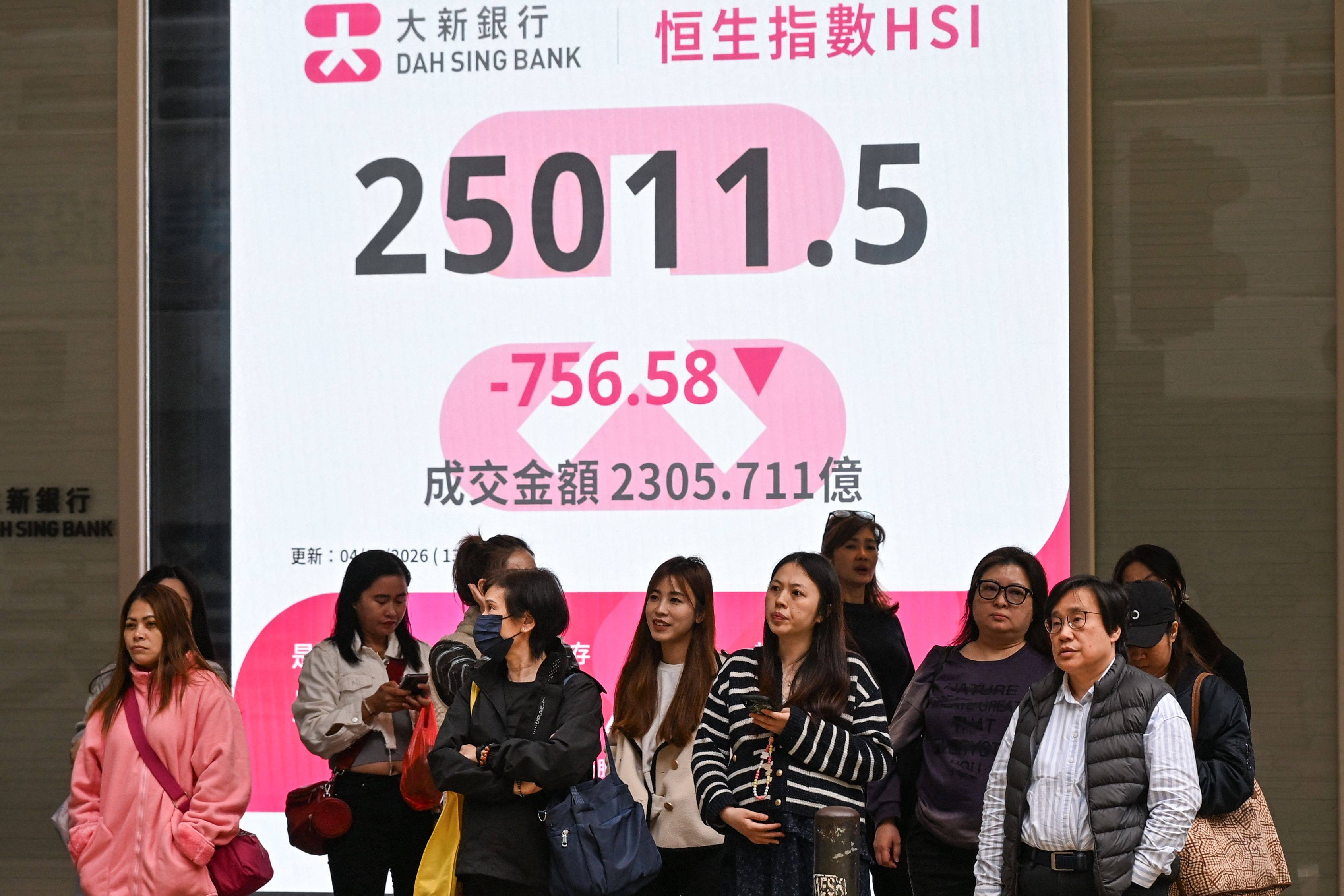People wait to cross a road in front of a sign showing the Hang Seng Index in Hong Kong on March 4. Photo: AFP