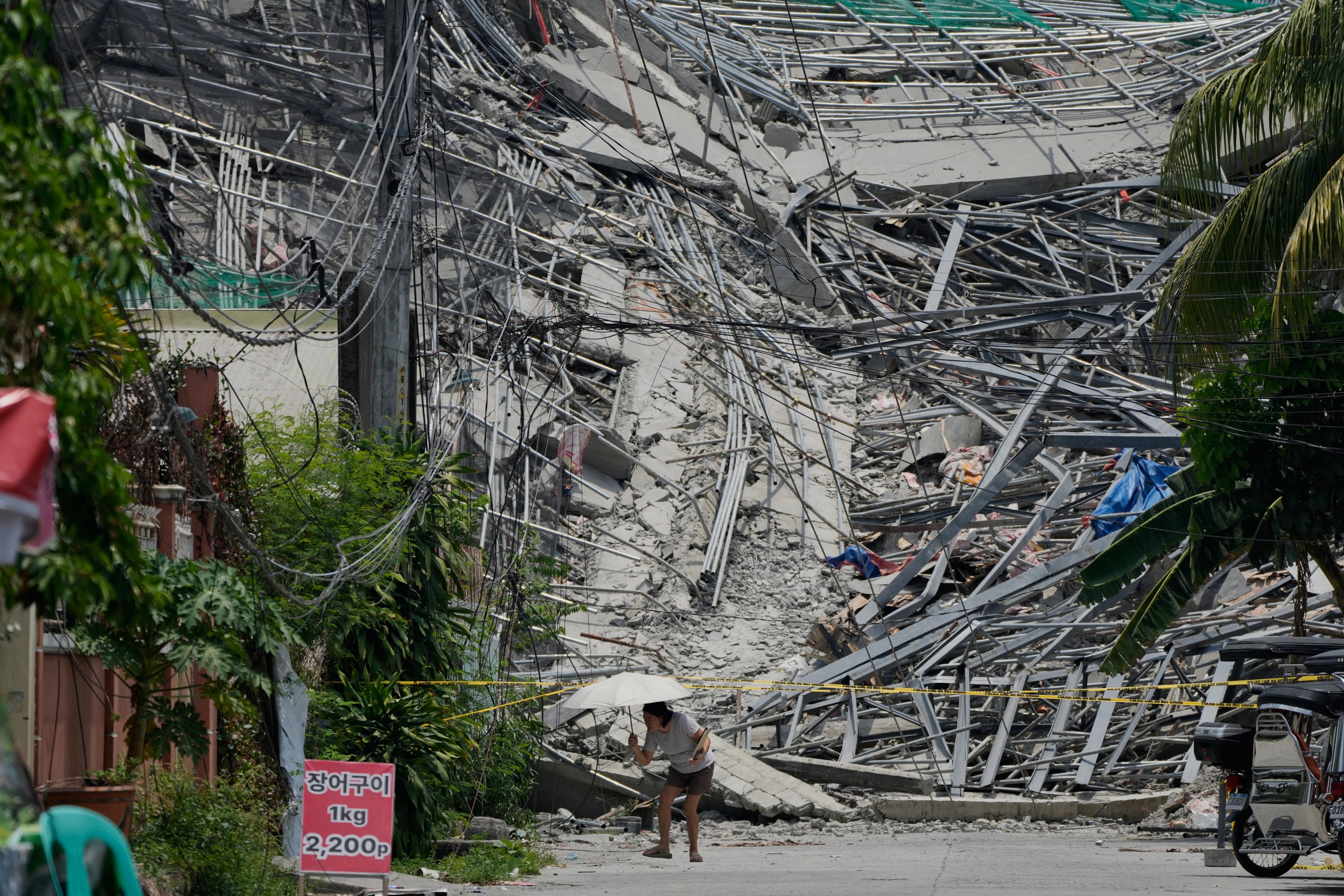 A woman walks beside a collapsed building where nearly 20 people are believed to be trapped in Angeles city in Pampanga province, north of Manila, on Monday. Photo: AP