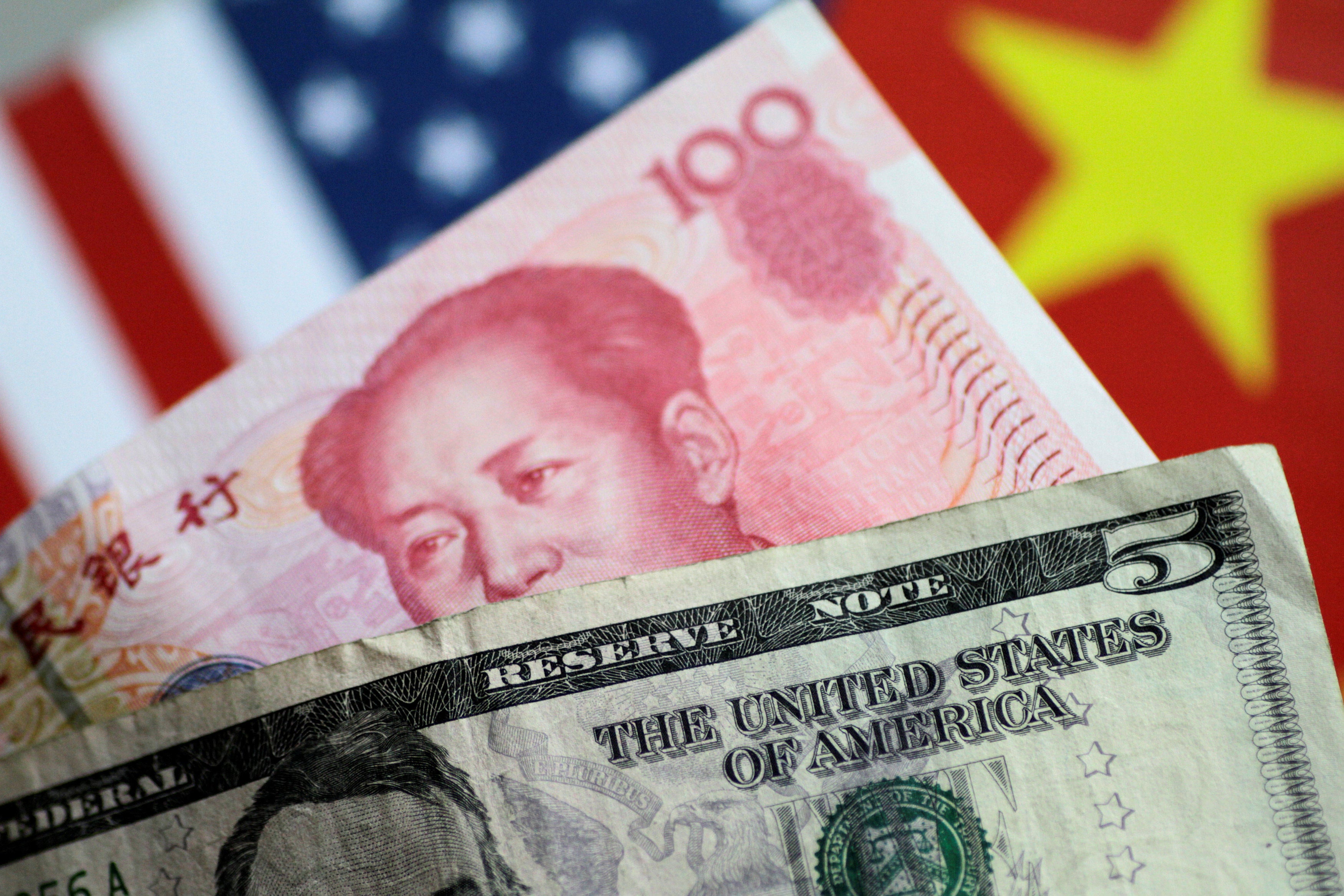 US dollar and Chinese yuan notes are seen with national flags in the backdrop. Photo: Reuters