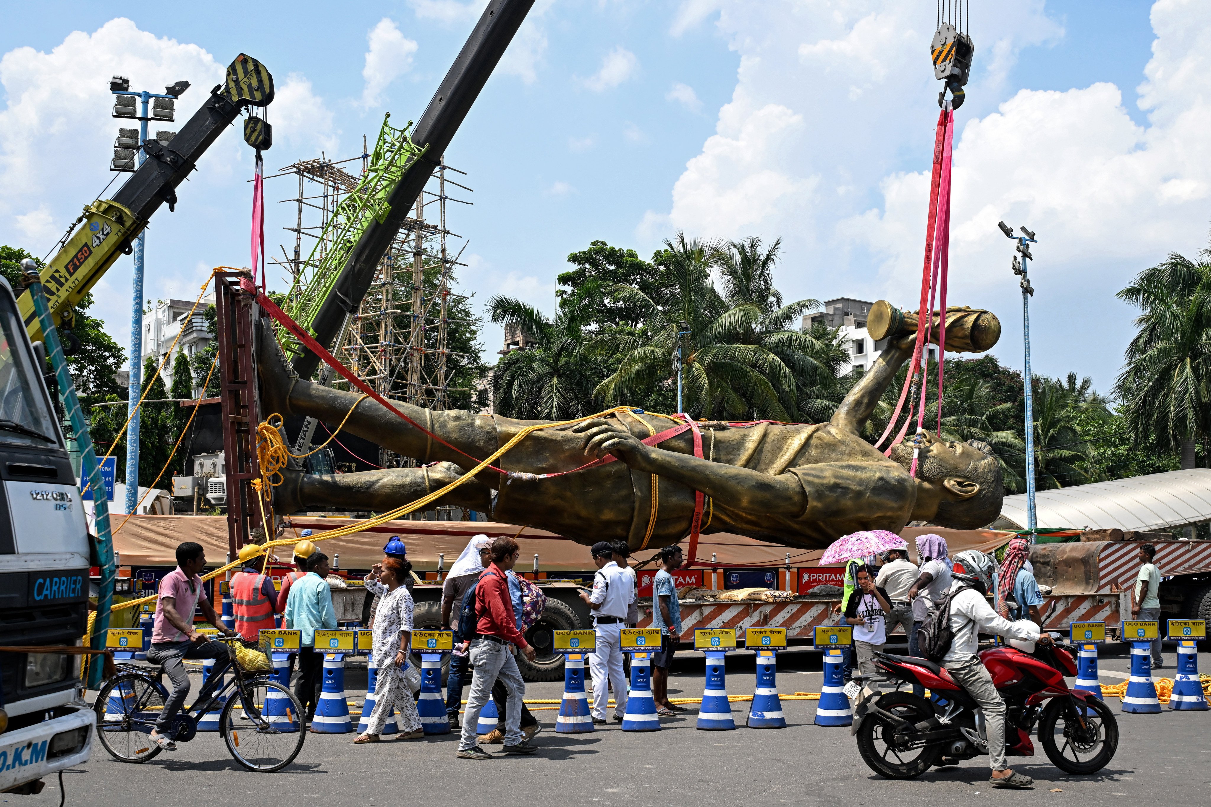 Pedestrians watch as workers remove a statue of Argentine football player Lionel Messi for its re-installation to a safer place in Kolkata on June 1, 2026. A giant statue of football superstar Lionel Messi erected in India to mark his visit last year is “swaying in the wind” and will be removed, a lawmaker told AFP on May 27. (Photo by Dibyangshu SARKAR / AFP)