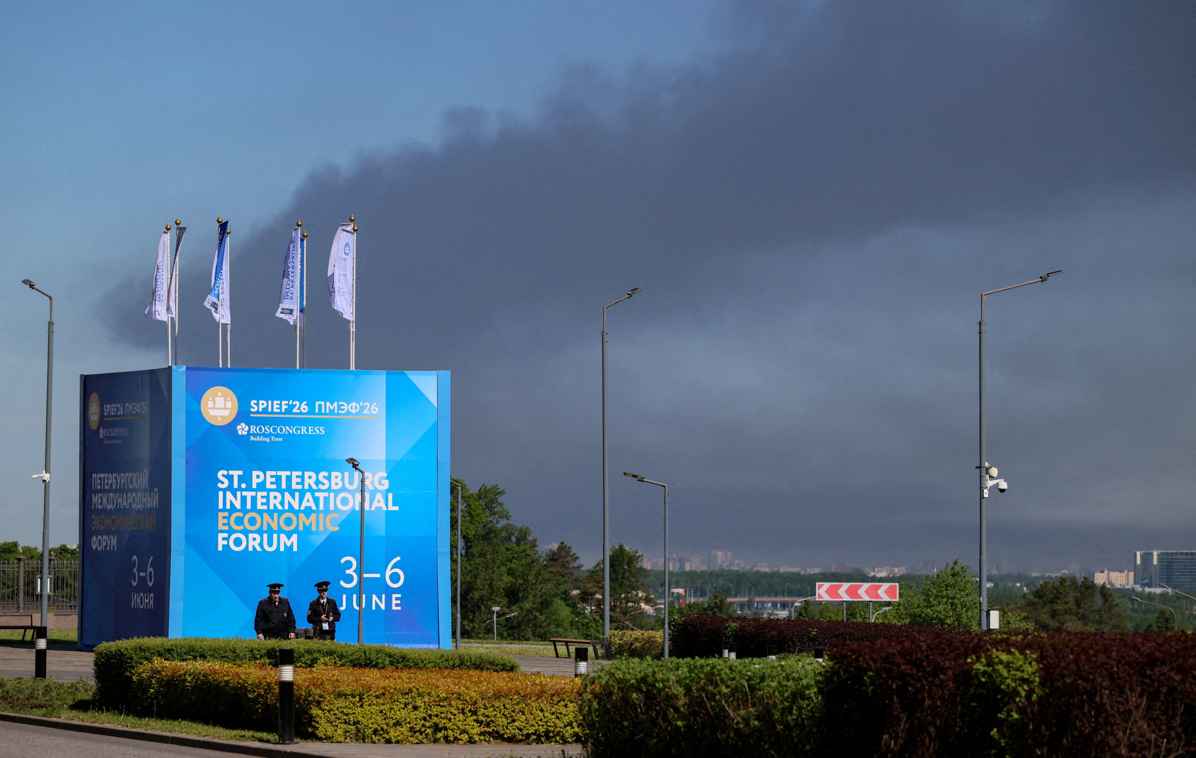 Police officers stand in front of a banner and flags with the logo of the Saint Petersburg International Economic Forum as heavy smoke billows in the background after Ukrainian drones hit infrastructure on Wednesday. Photo: Reuters