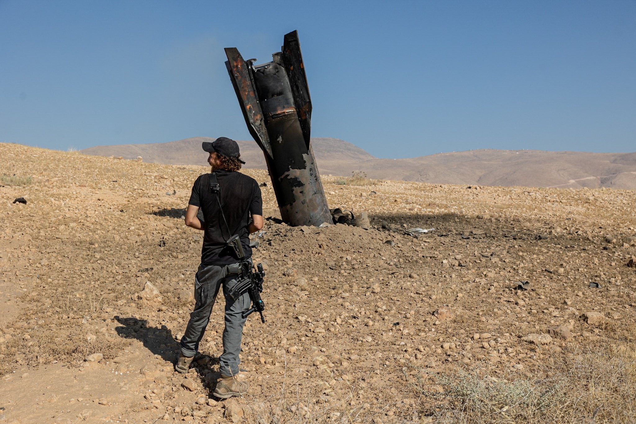 An Israeli settler stands next to part of a missile protruding from the ground, following strikes from Iran, in the central Israeli-occupied West Bank. Photo: Reuters