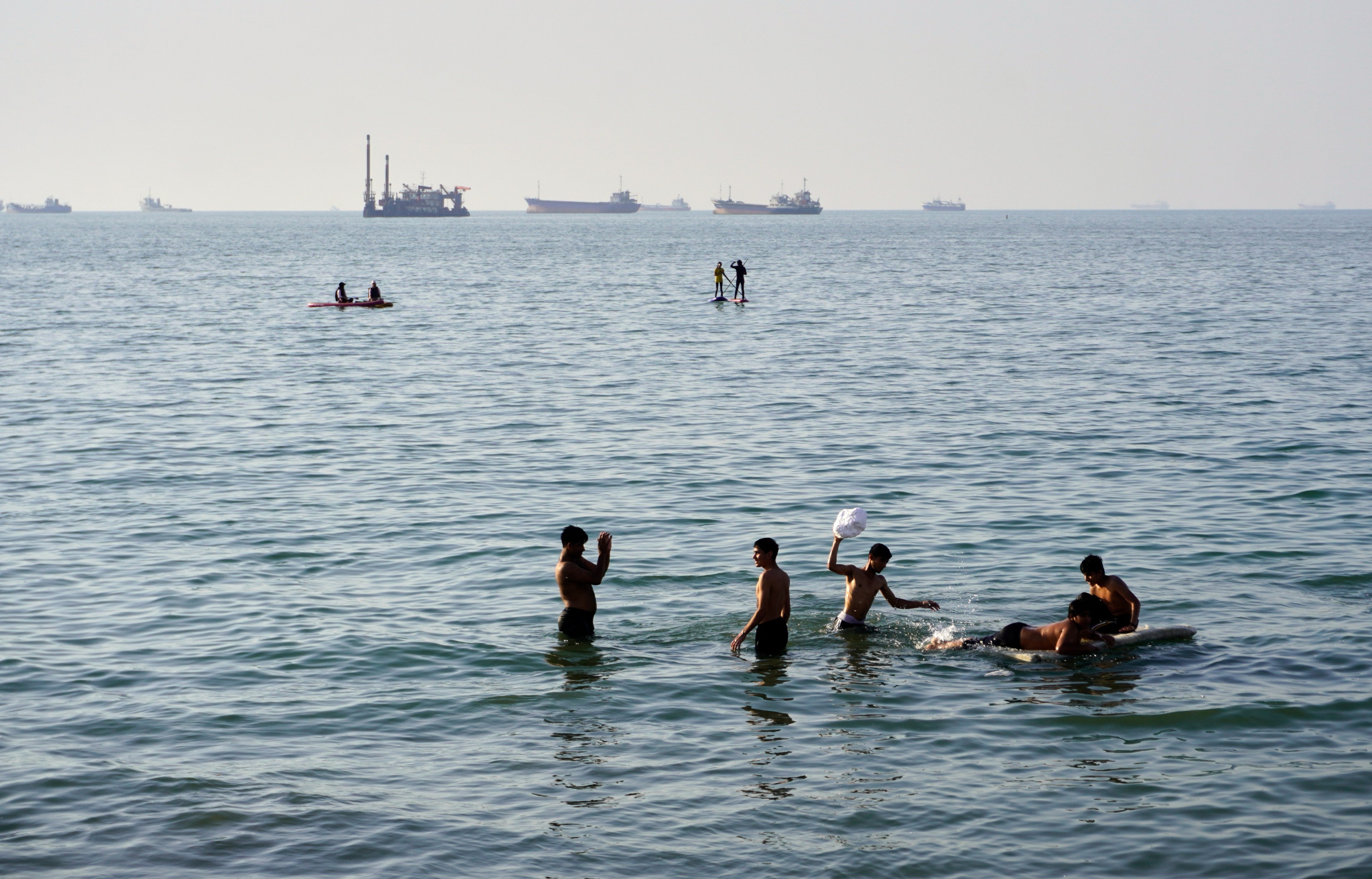 Residents swim and play in the waters of the Strait of Hormuz while ships lie anchored in the distance off Bandar Abbas, Iran, on Wednesday. Photo: ISNA via AP