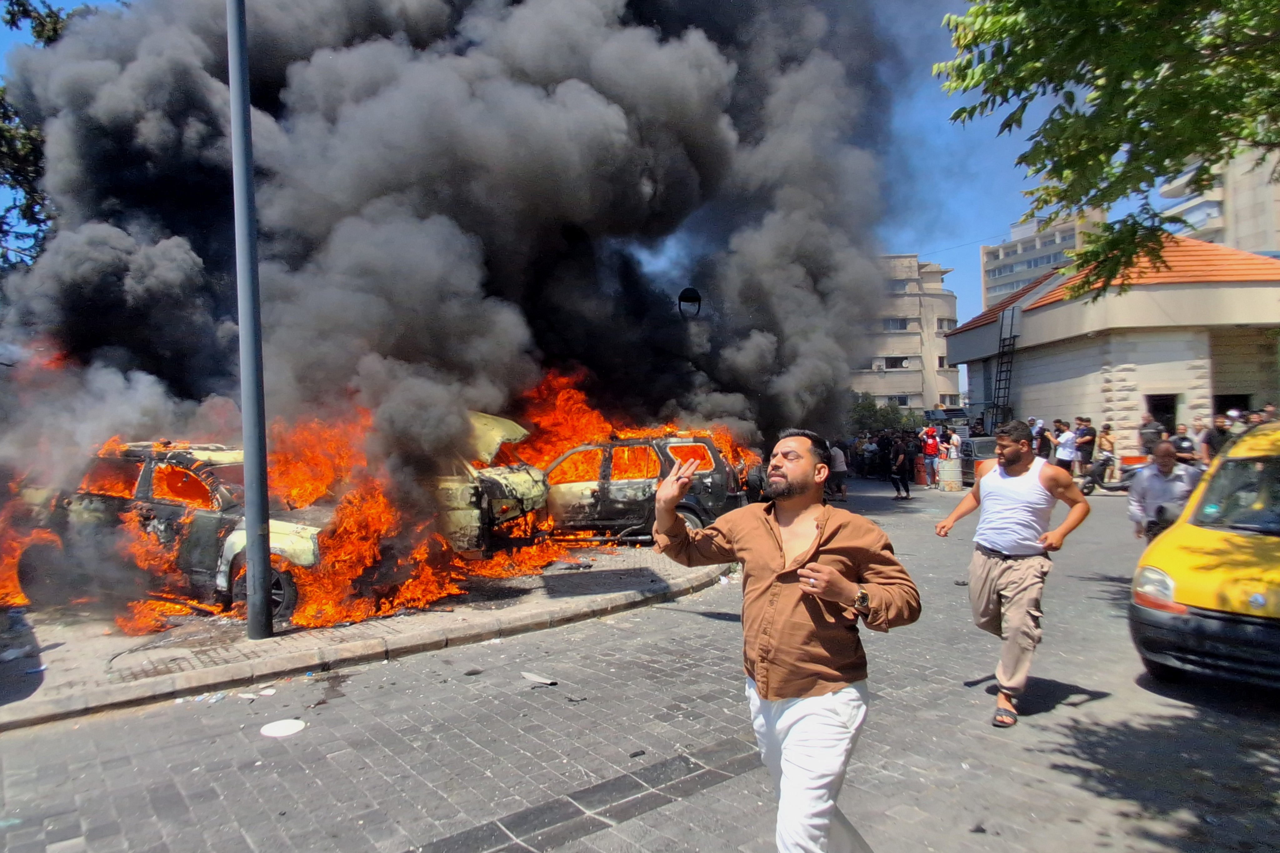 People run in front of burned cars that were attacked in an Israeli airstrike in the southern port city of Sidon, Lebanon, on Wednesday. Iran is demanding Israel end a campaign against Hezbollah in Lebanon as part of concluding its war. Photo: AP