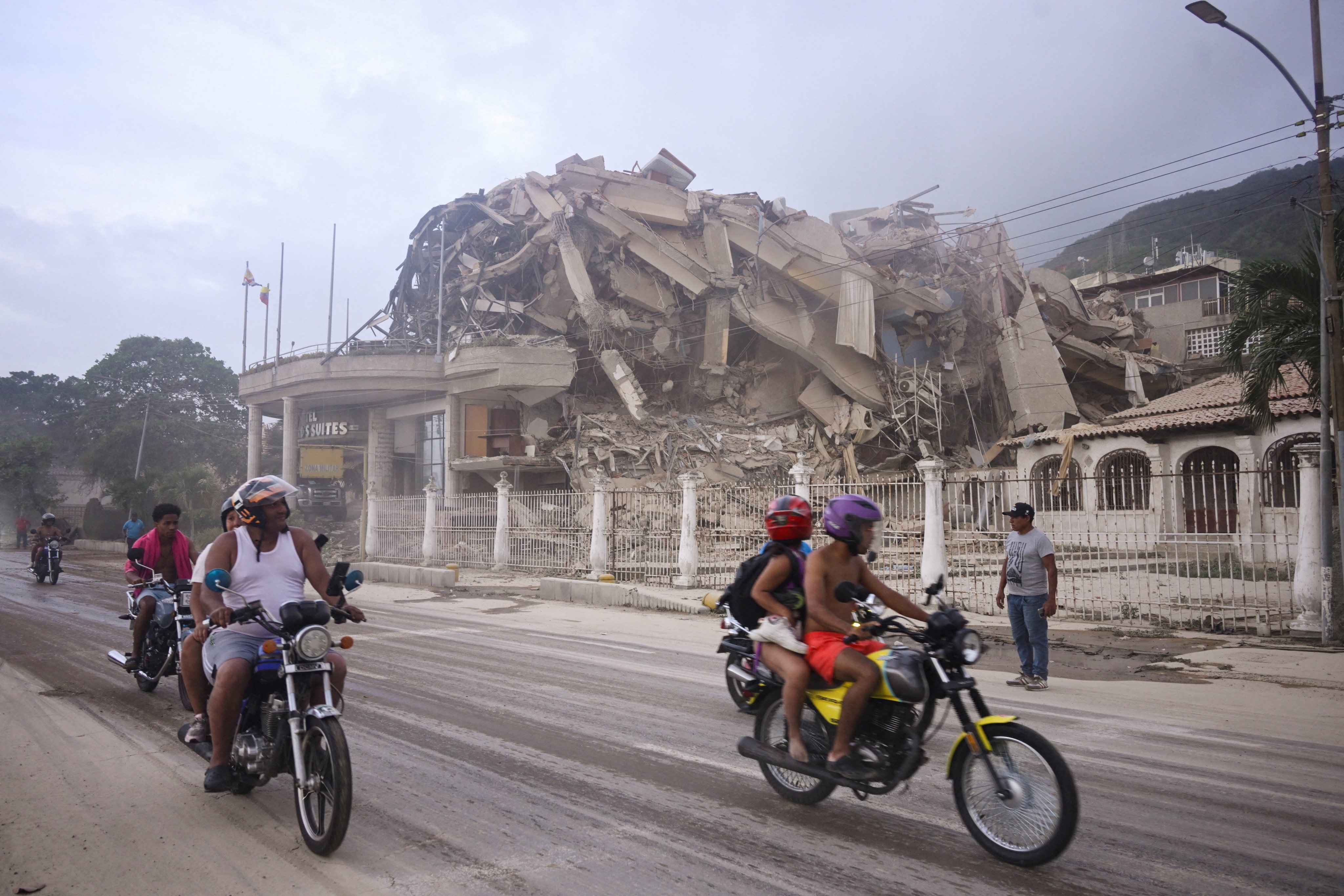 People ride past a collapsed building in La Guaira. Photo: Reuters