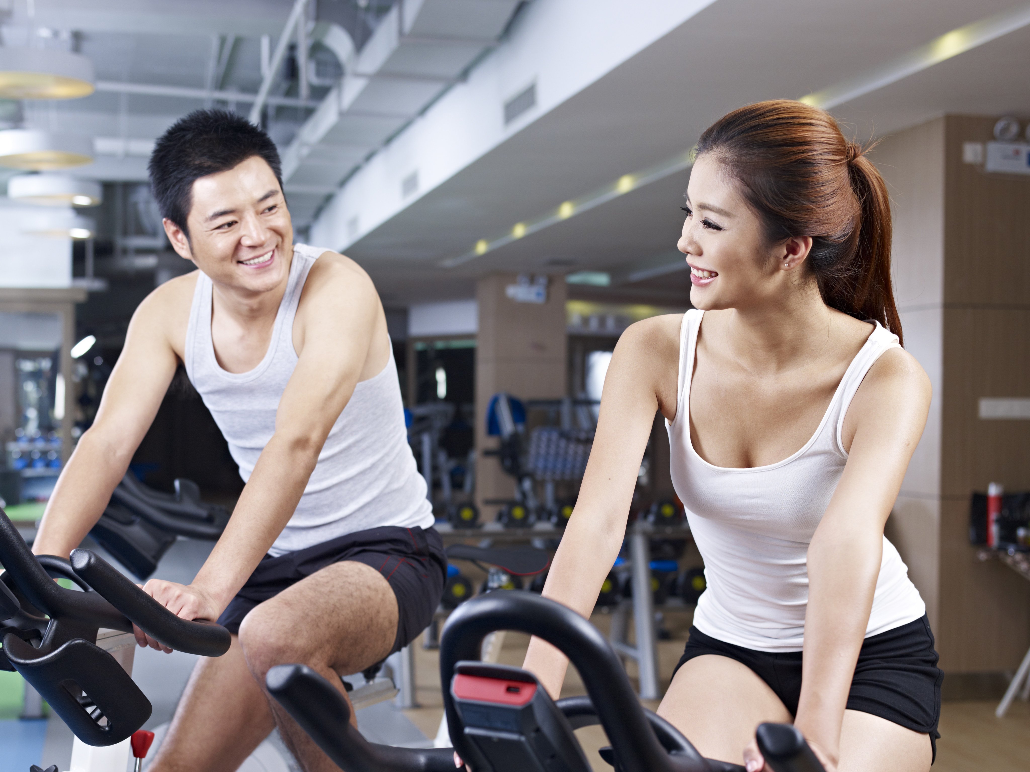 young man and woman talking while exercising on bicycle in fitness center.

Credit: Shutterstock
