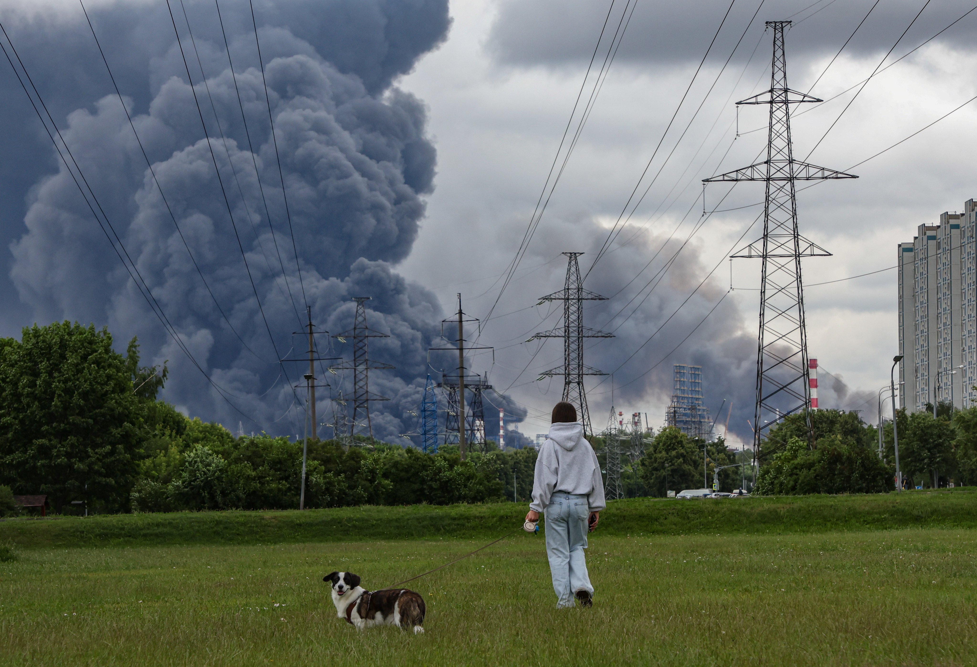 A woman and her dog walk in a park as smoke billows in the background following a reported Ukrainian drone attack in Moscow on June 18. Photo: EPA