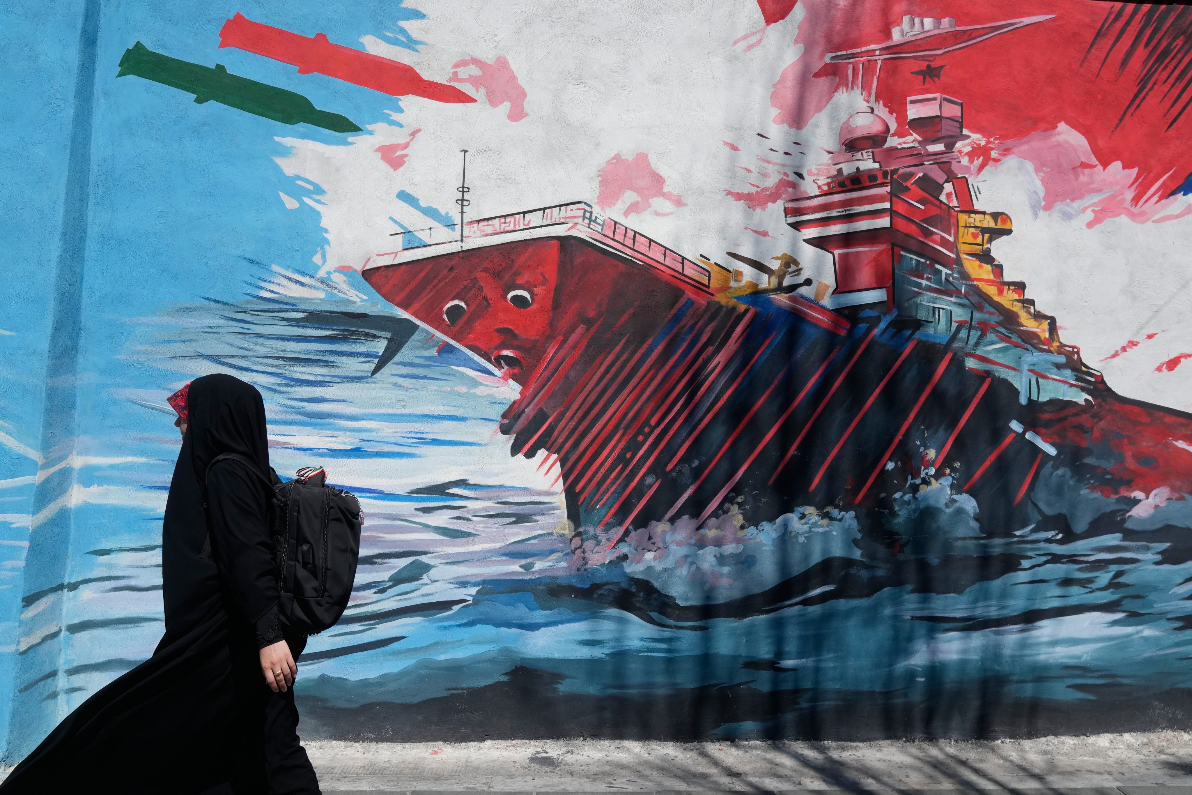 A woman walks past a mural depicting a US aircraft carrier under missile attack in downtown Tehran, Iran, on June 8. Photo: AP
