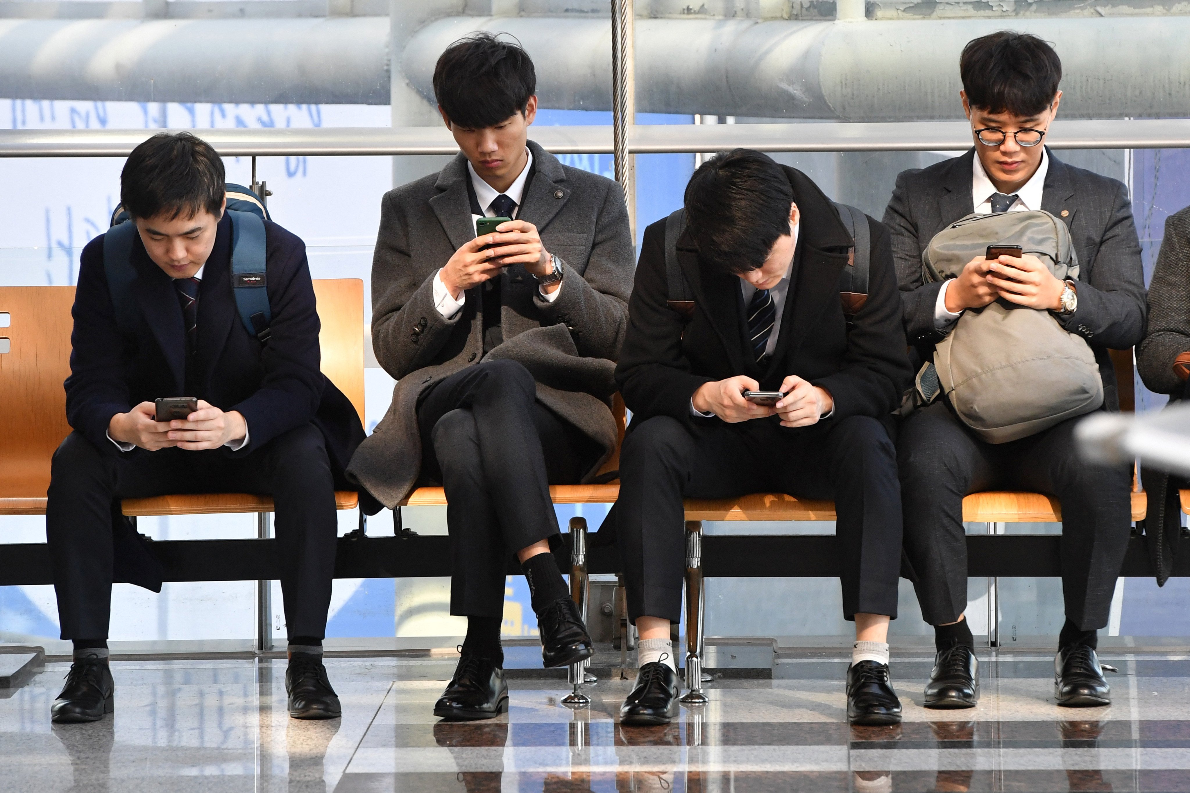 Men look at their smartphones while waiting in Seoul. Photo: AFP