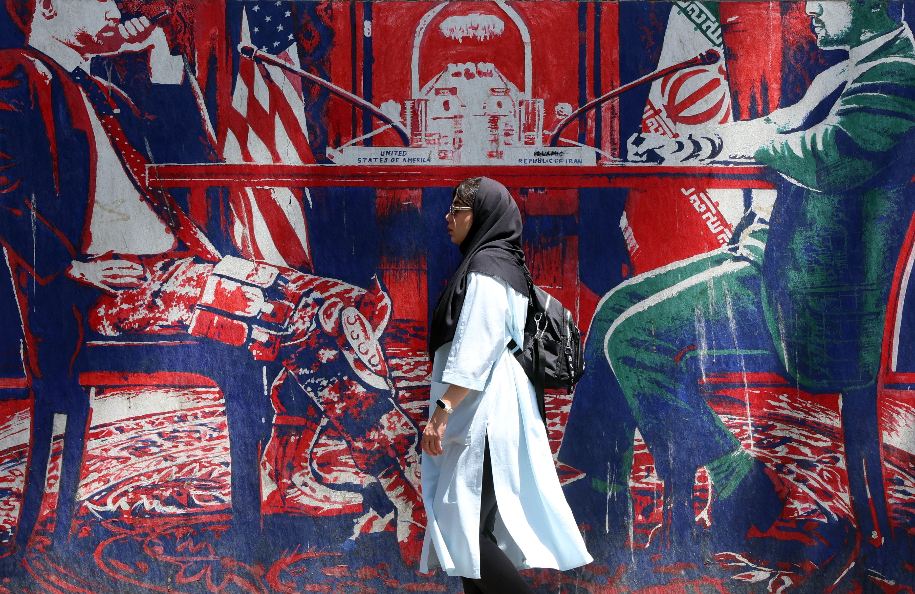 An Iranian woman walks past an anti-US mural, depicting an Iranian and US negotiation table, next to the former US embassy in Tehran, Iran, on June 22. Photo: EPA