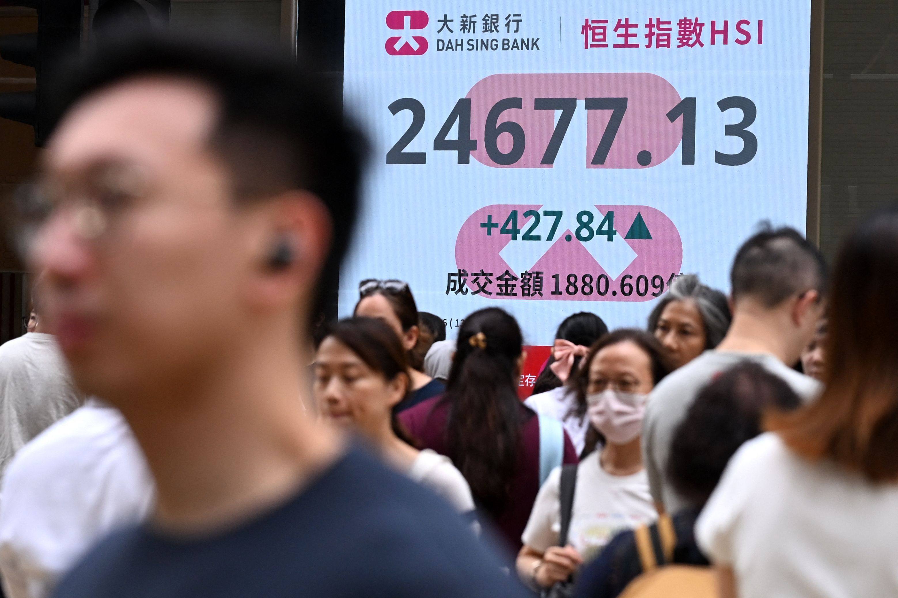 Pedestrians walk across a street next to an electronic sign board showing the Hang Seng Index in Hong Kong on June 12. Photo: AFP