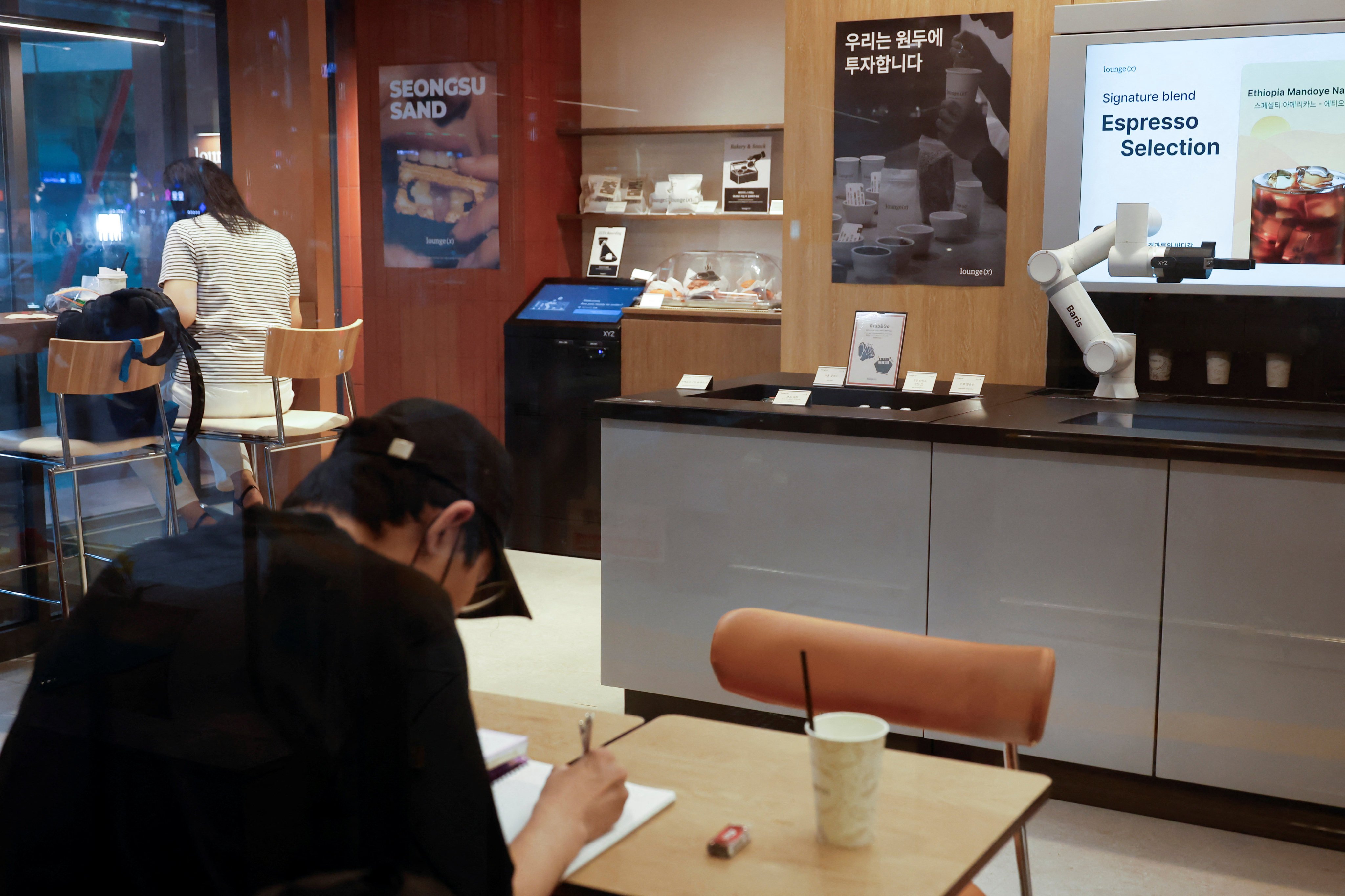 People sit inside an unstaffed cafe where a robot arm prepares coffee in Seoul on June 19. Photo: Reuters