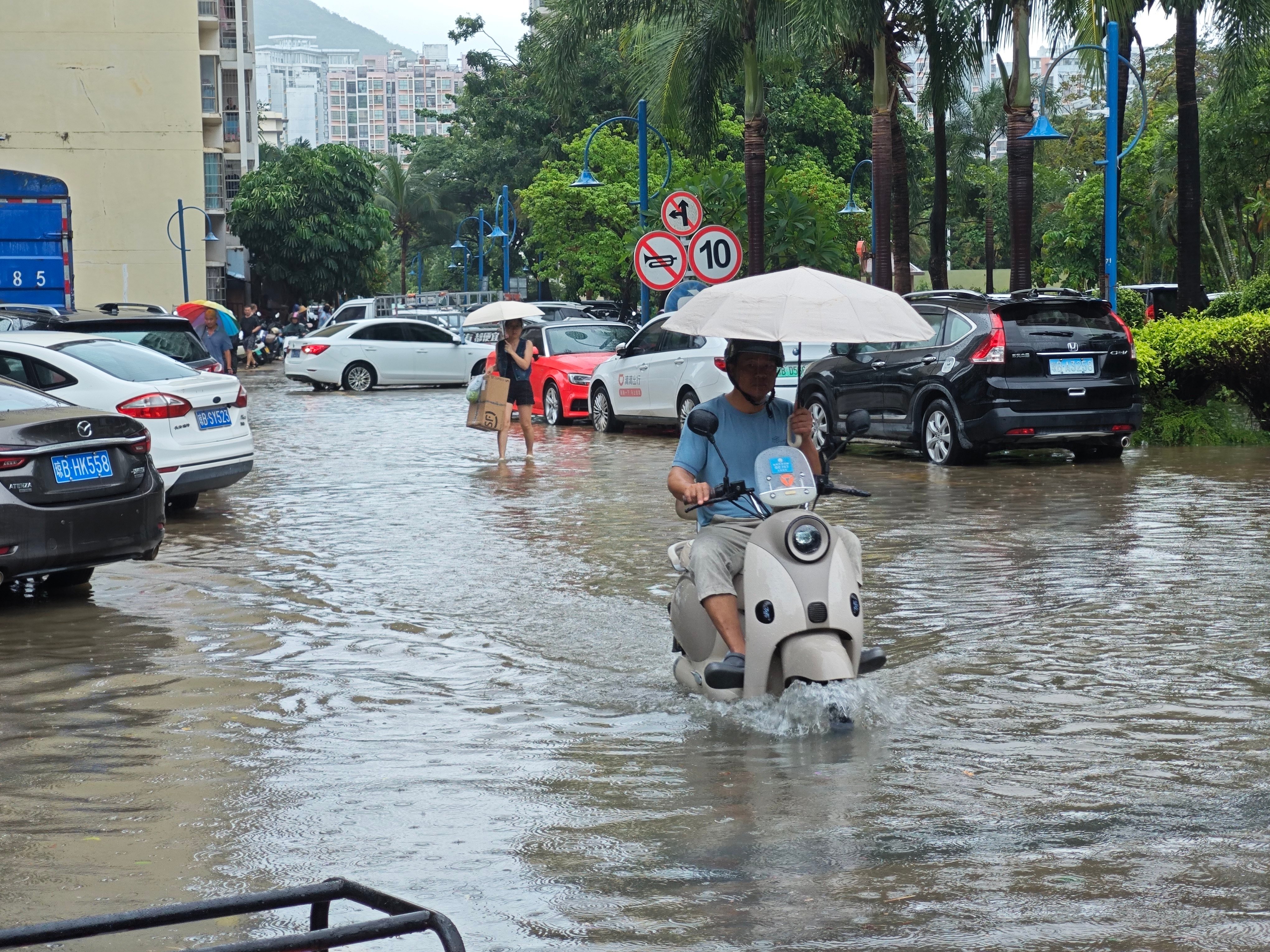 SANYA, CHINA - JULY 04: Residents ride through waterlogged road in a residential compound as typhoon Maysak brings torrential rains and wind to the area on July 4, 2026 in Sanya, Hainan Province of China. Typhoon Maysak, the 10th typhoon of the year, made landfall on the coast of south China’s Hainan Province on evening of July 3, bringing torrential rains that flooded multiple roads in the coastal city of Sanya. (Photo by Zhang Yuehe/China News Service/VCG )No Use China.