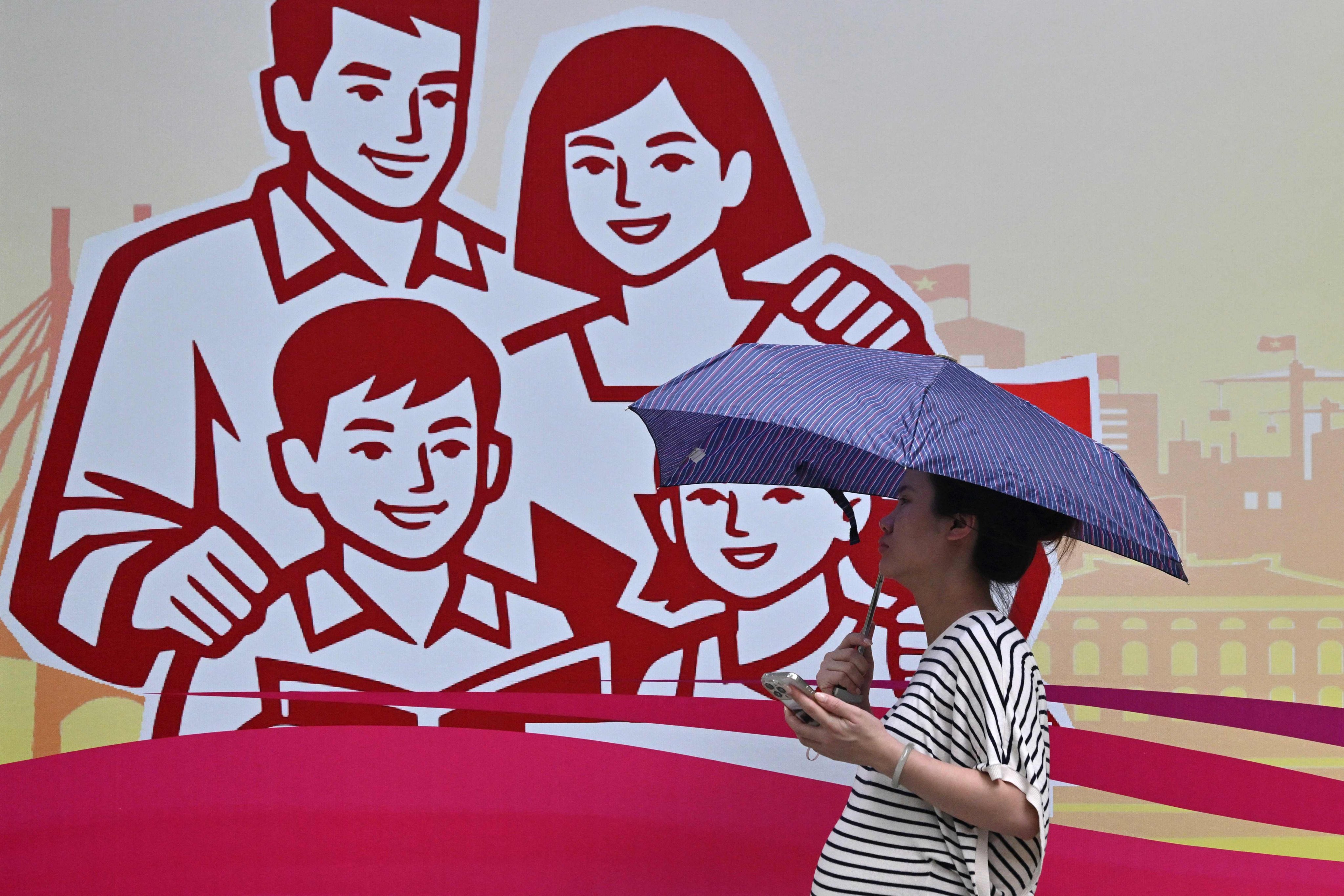 A pregnant woman holding an umbrella walks past a billboard of a happy family in Hanoi last month. Photo: AFP