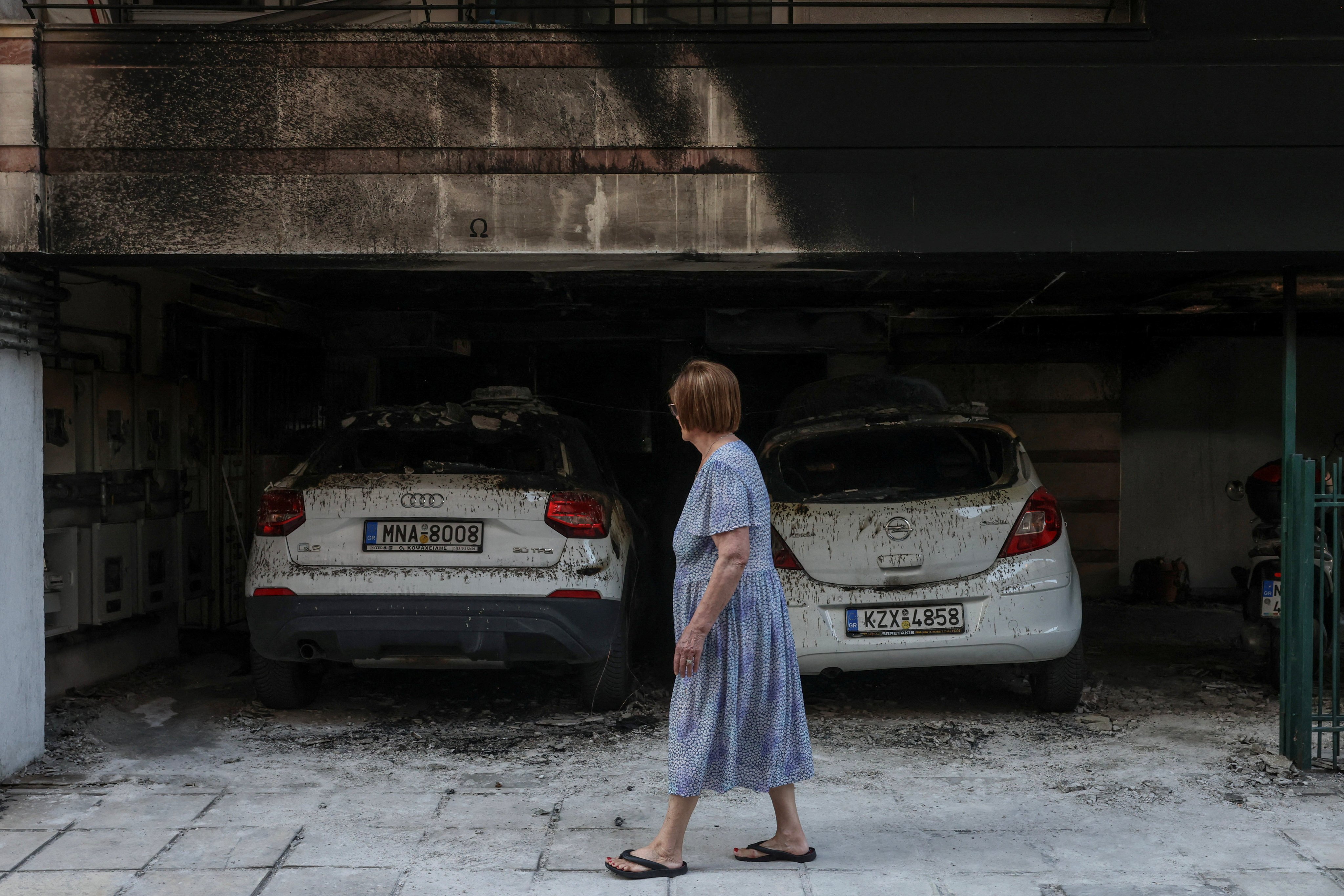 A woman walks past damaged cars and a building after attackers firebombed three residential buildings linked to Greece’s governing party in the northern city of Thessaloniki, Greece on July 1. Photo: Reuters