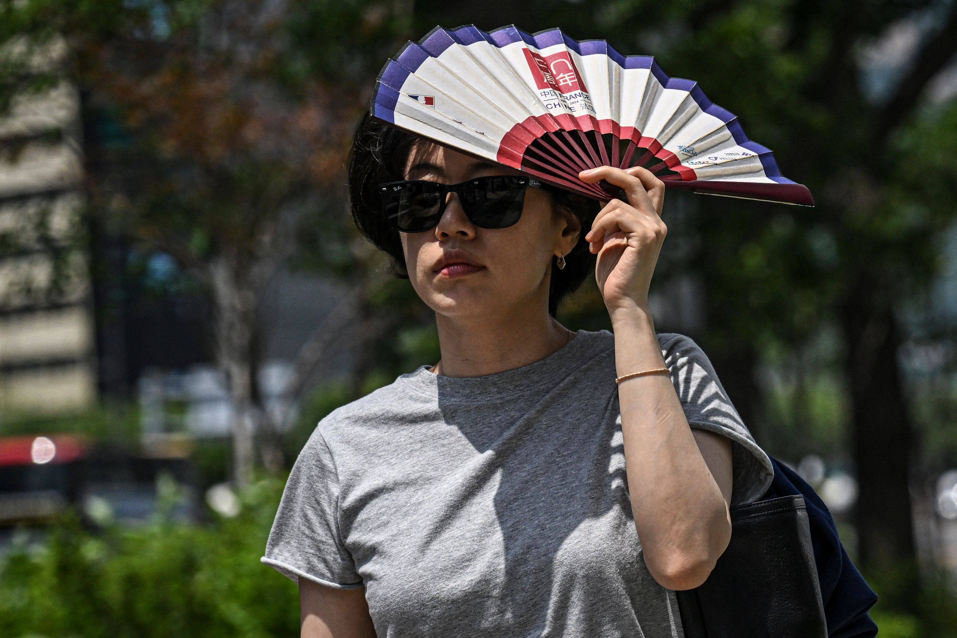 A woman uses a fan to shelter from the sun on a street in Seoul Sunday. Photo: AFP