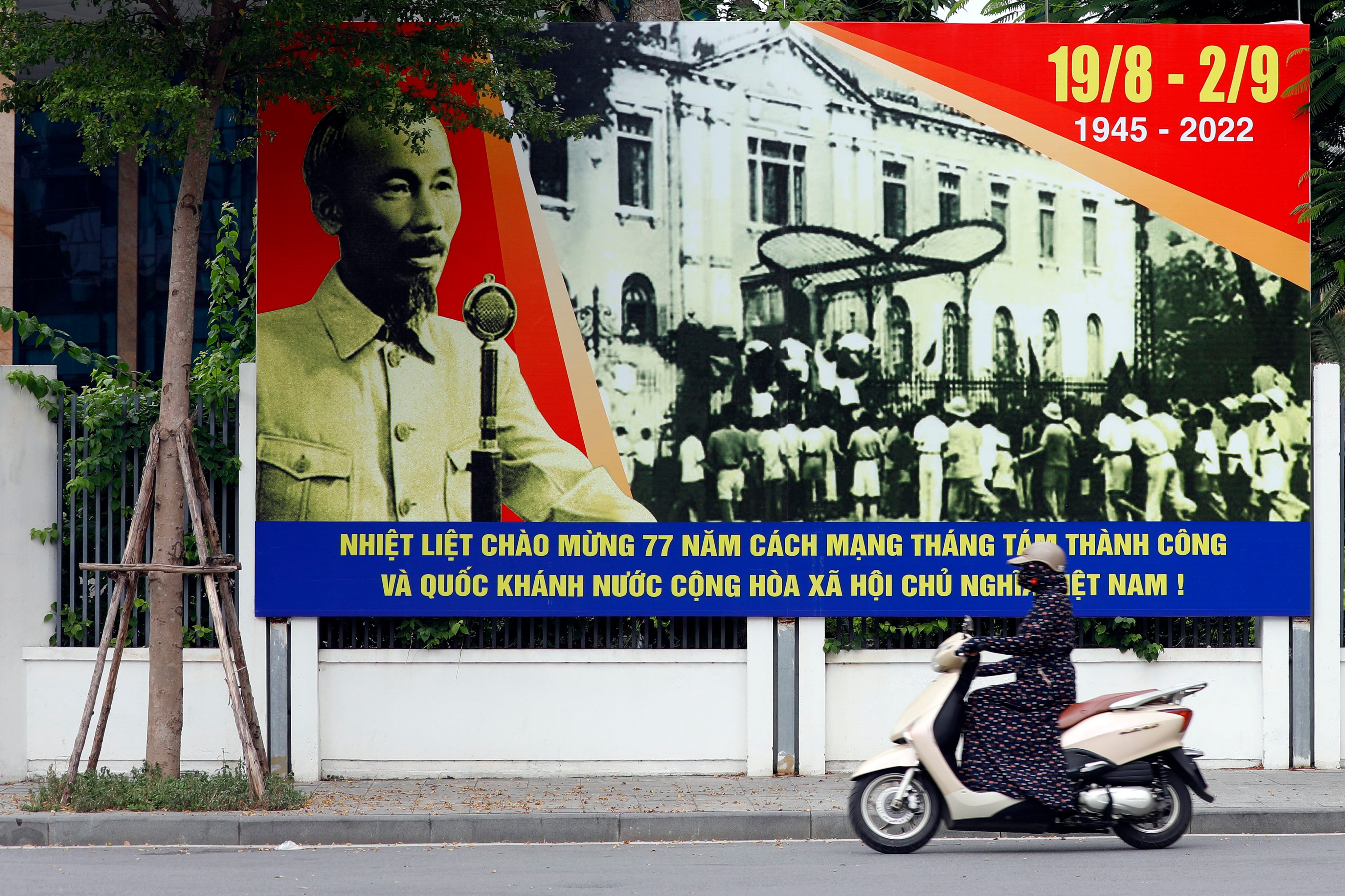 A woman rides a motorbike past a poster with a portrait of the late former president Ho Chi Minh in Hanoi on August 31, 2022. Photo: EPA-EFE