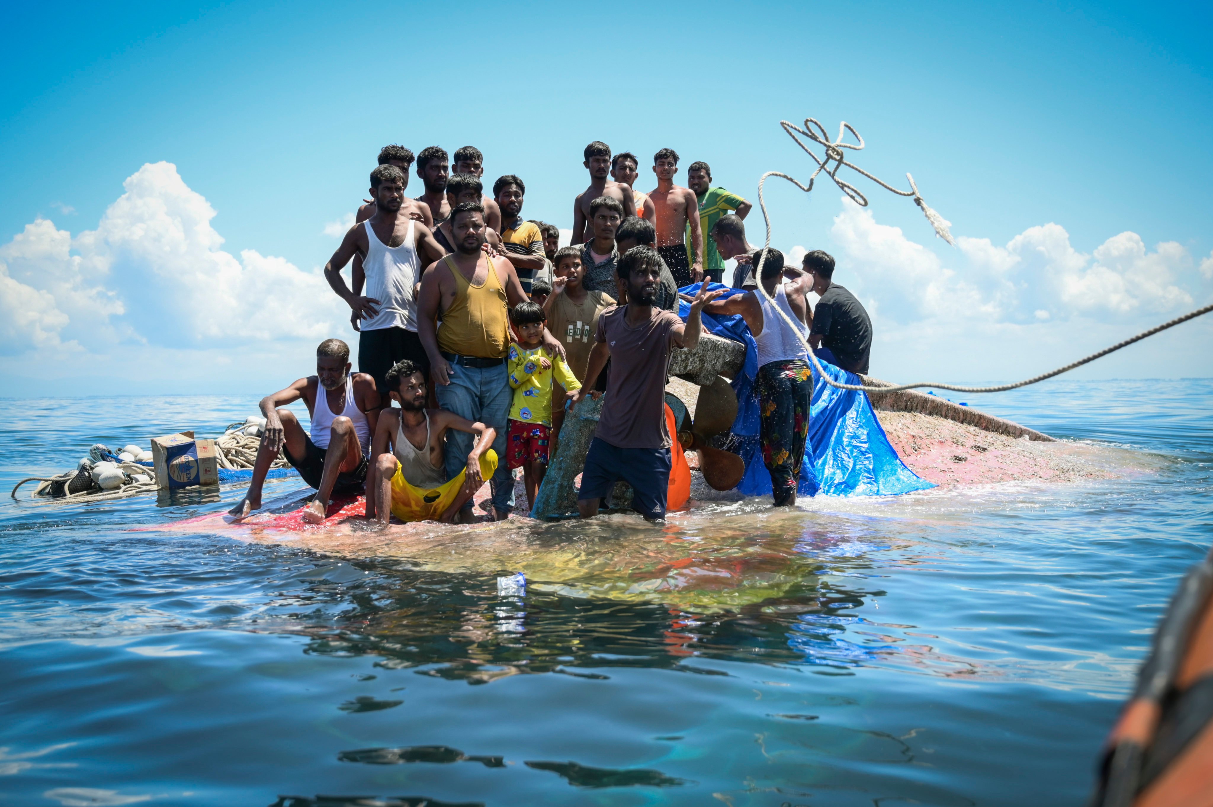 Rohingya refugees stand on their capsized boat as rescuers throw a rope to them off West Aceh, Indonesia, in 2024. Photo: AP