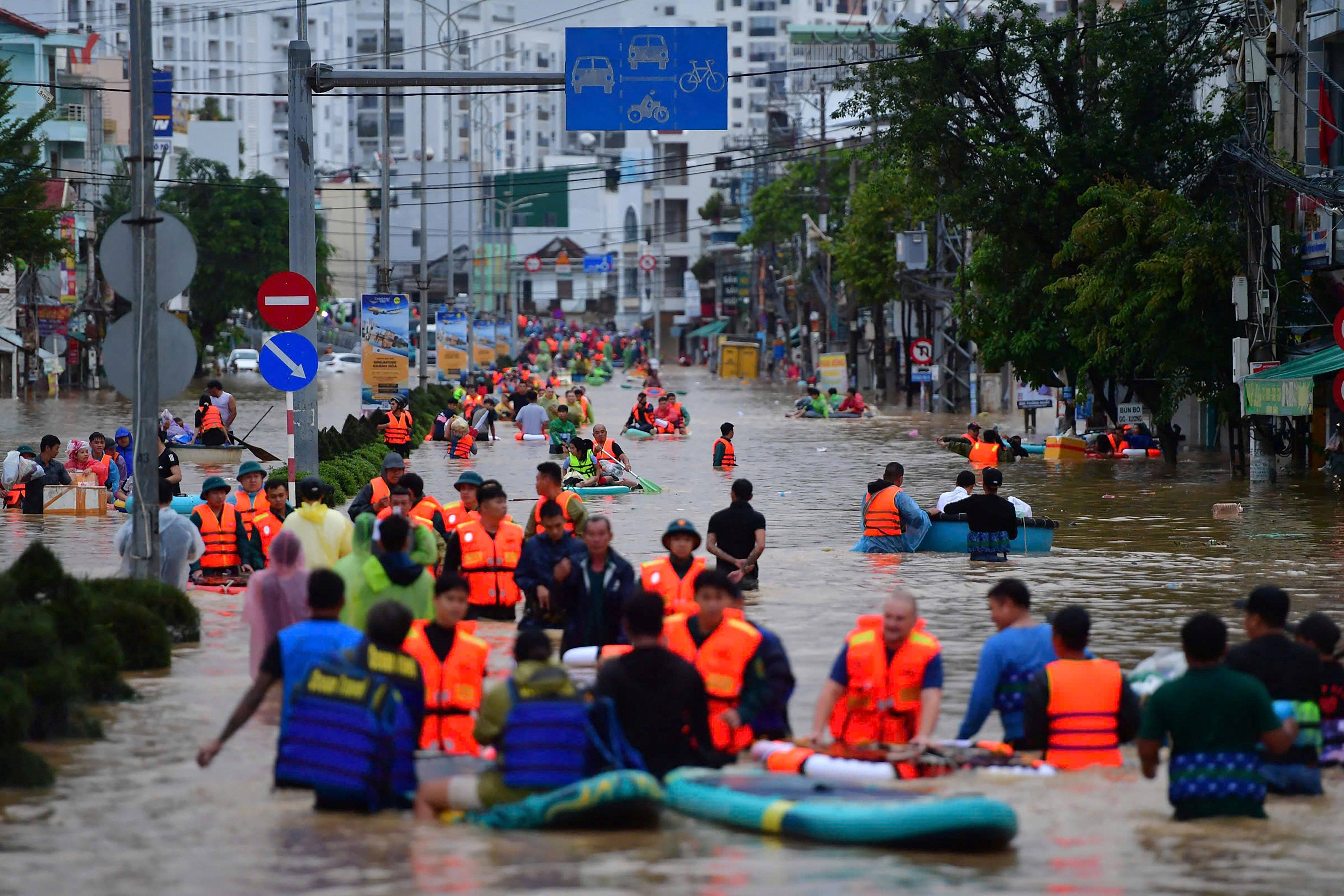 TOPSHOT - This photo taken on November 20, 2025 shows people wading through floodwaters in Nha Trang in Vietnam's coastal province of Khanh Hoa. Rescuers raced to find more than a dozen people still missing on November 22 after a week of heavy flooding in Vietnam, where authorities said at least 55 people have died. (Photo by Duc Thao / AFP)