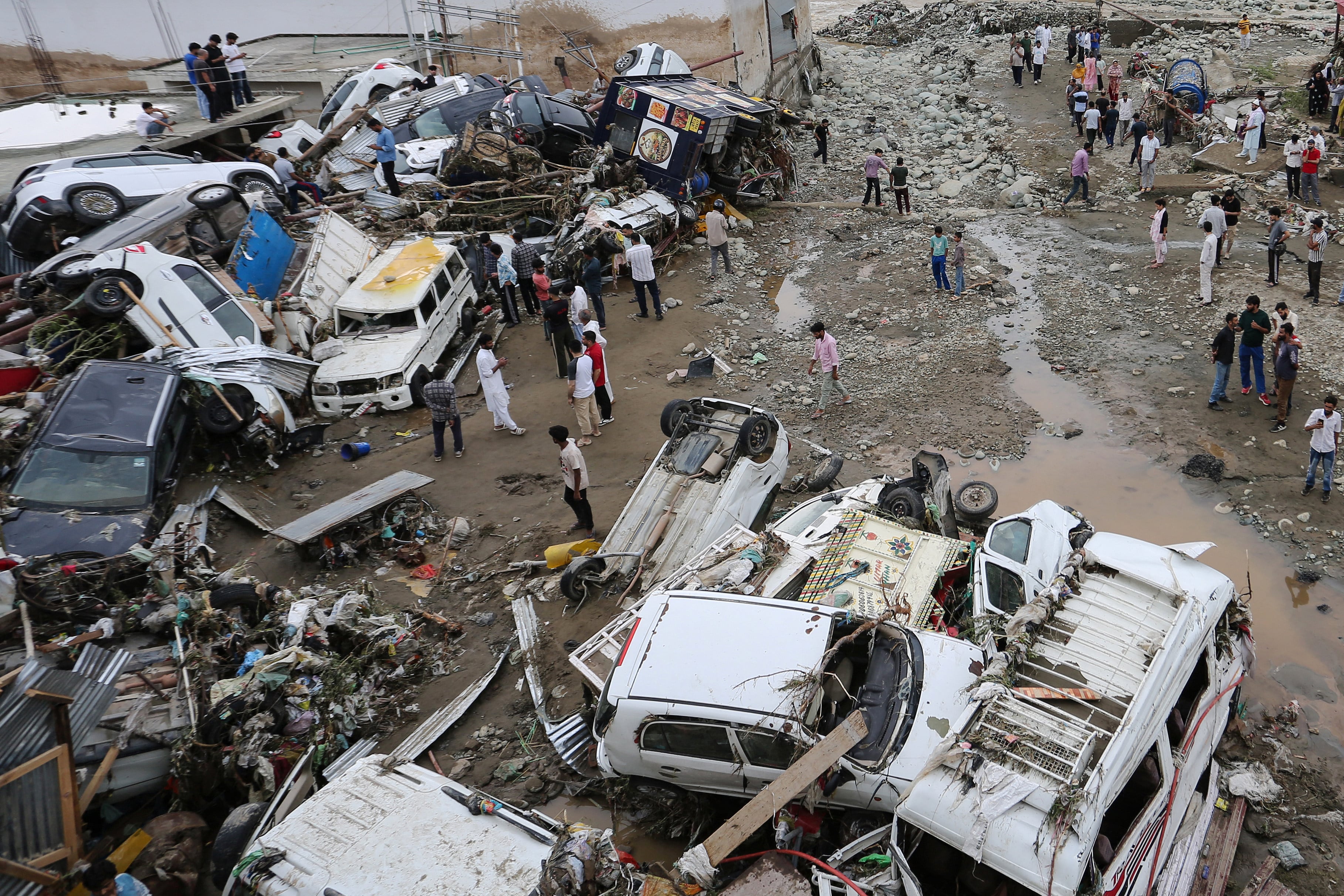 Residents look at damaged vehicles after flash flood and landslide triggered by heavy rains wreaked havoc at Rajouri district in India’s Jammu region on July 19, 2026. Flash floods and landslides caused by monsoon rains killed at least 19 people in India on July 19, officials and local media said, as authorities mounted rescue operations in affected regions. (Photo by Mir Imran / AFP) / ALTERNATIVE CROP