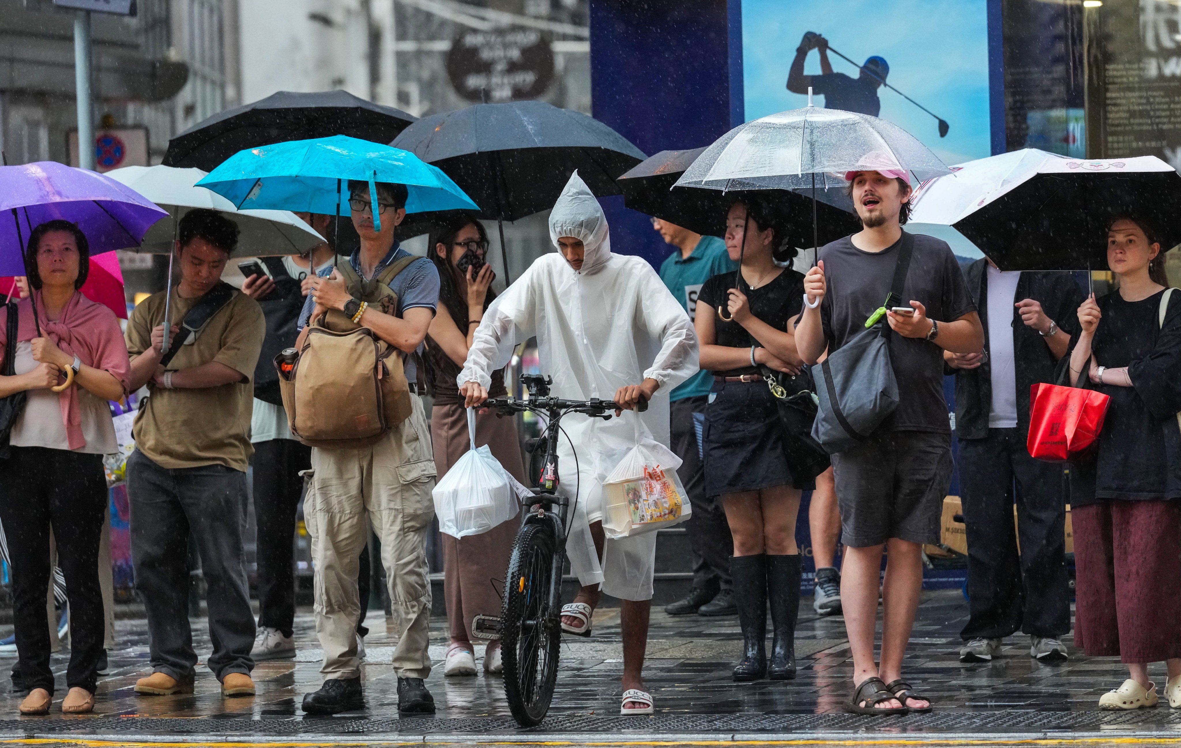 People wait to cross the road in Tsim Sha Tsui during heavy rain on July 16. For delivery workers and part-timers, income is tied directly to hours worked and work suspensions during extreme weather can mean immediate financial hardship. Photo: Jelly Tse