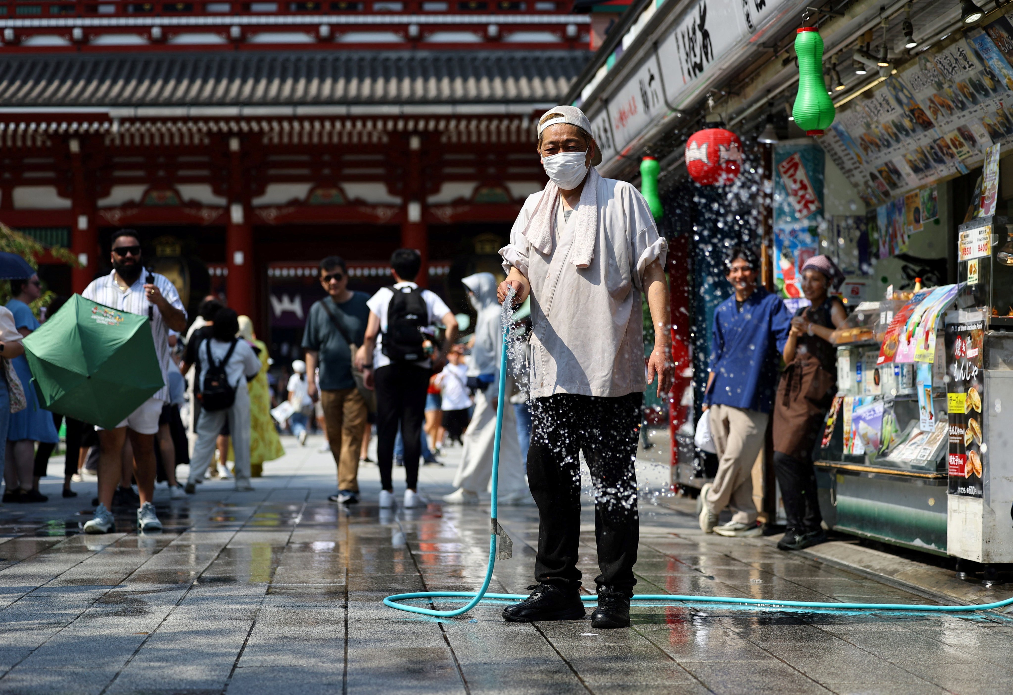 A traditional fast food shop worker conducts 'Uchimizu', the splashing of water onto the hot street in summer which is an old Japanese tradition meant to cool down the air as the water evaporates, along Nakamise Street at the Asakusa district, a popular sightseeing spot, as the Japanese government issued a heatstroke alert in Tokyo and other prefectures due to a heatwave, in Tokyo, Japan July 22, 2026. REUTERS/Issei Kato