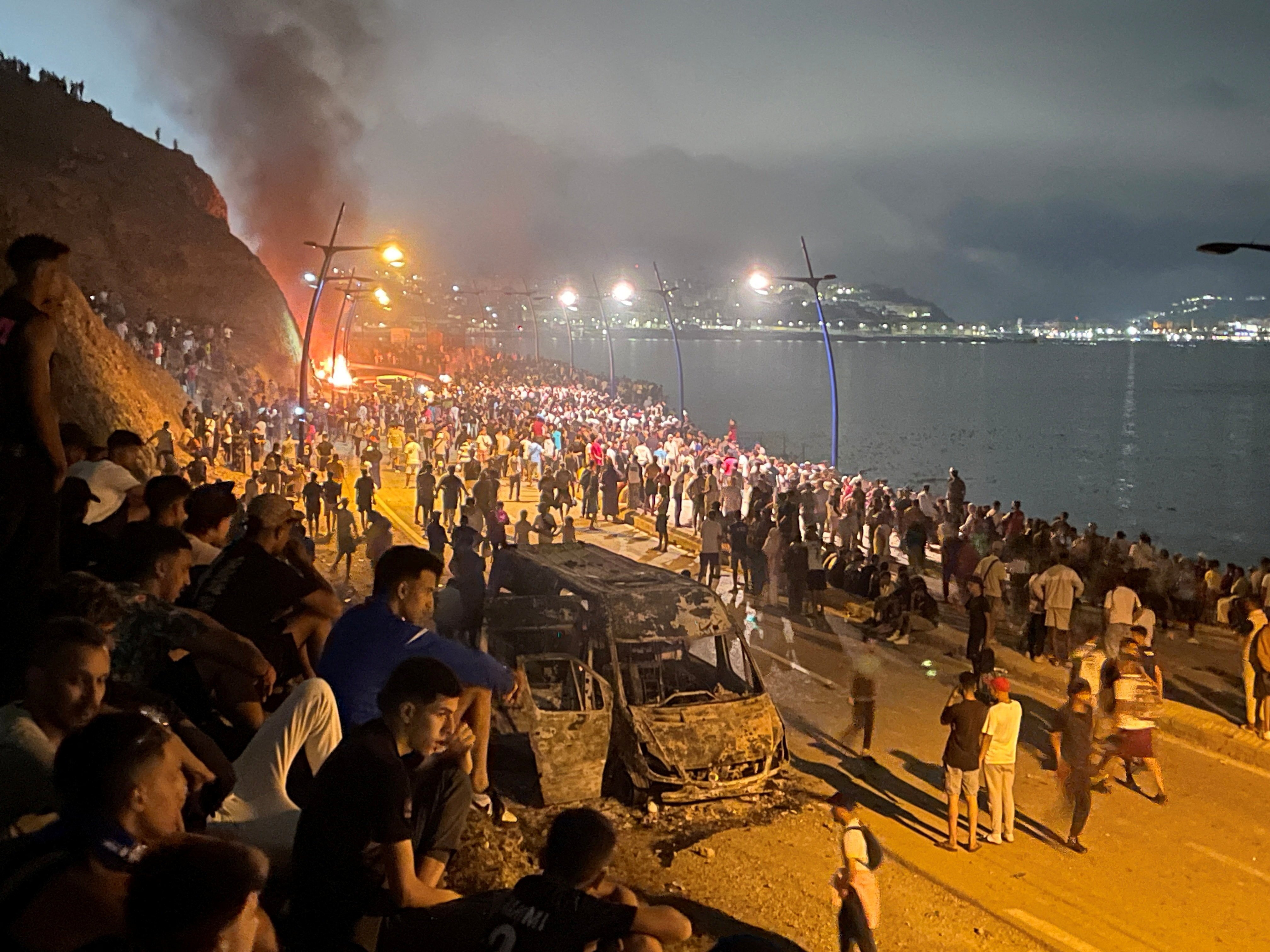 Migrants gather around a torched vehicle while waiting for a chance to cross to Ceuta, on the Moroccan side of the border in Fnideq. Photo: Reuters