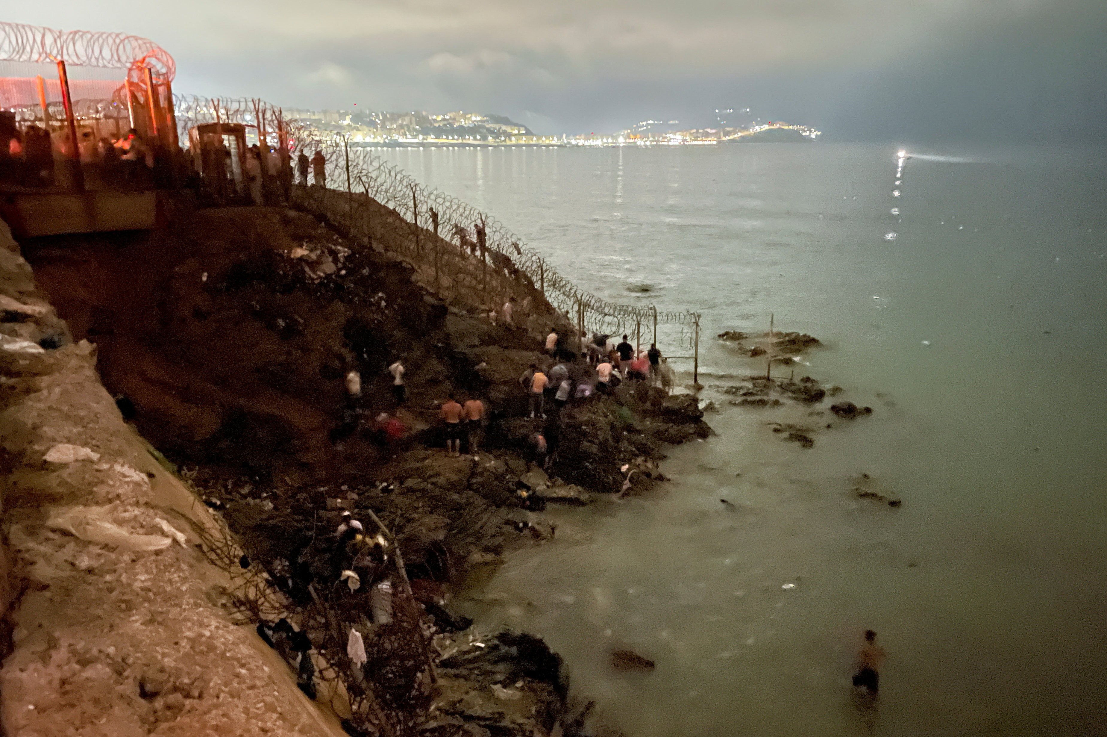 Migrants gather near a fence while waiting for a chance to cross to Ceuta. Photo: Reuters