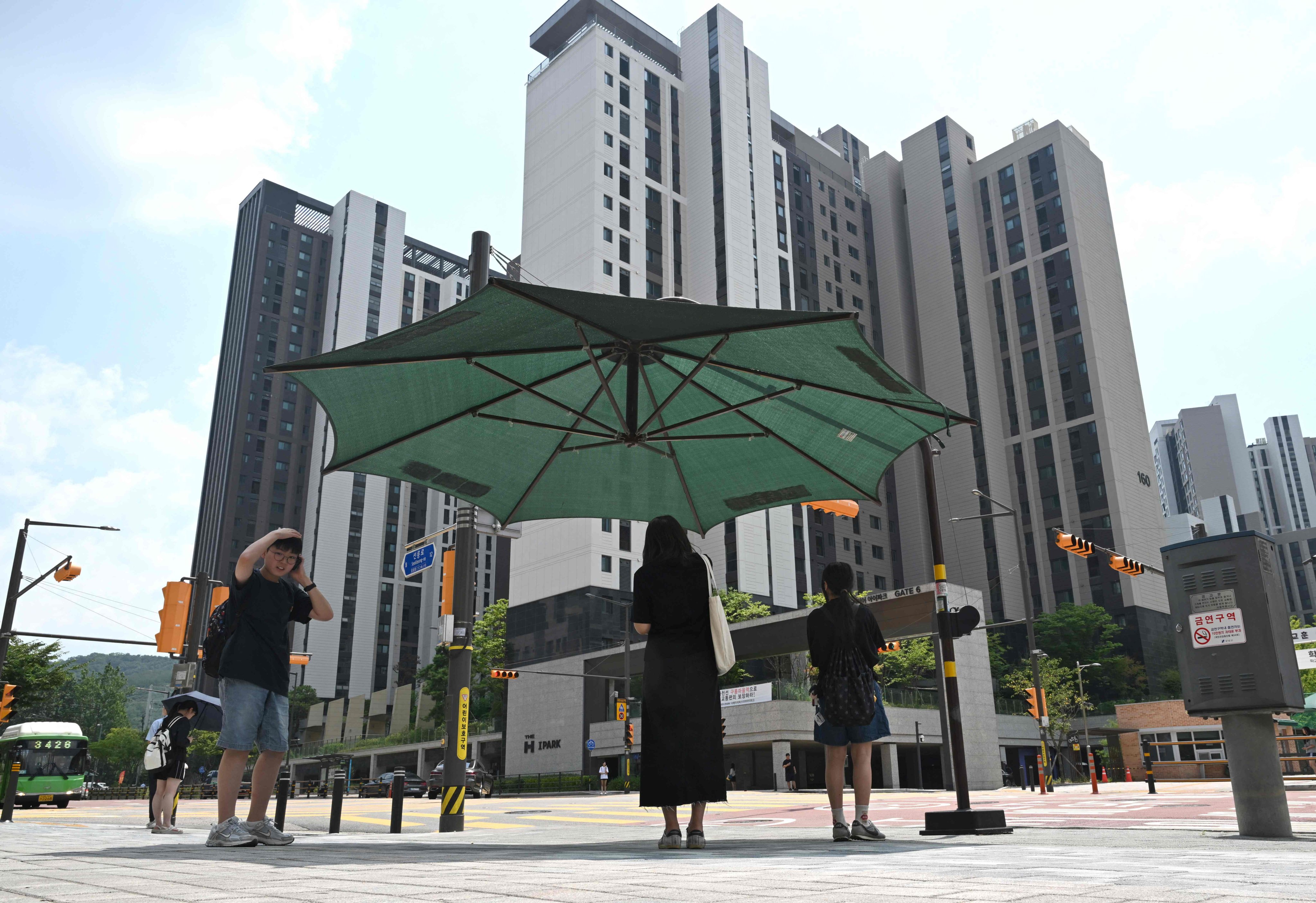 Pedestrians stand under a large umbrella at Gangnam district in Seoul on Tuesday as a record heatwave continues to grip South Korea. Photo: AFP