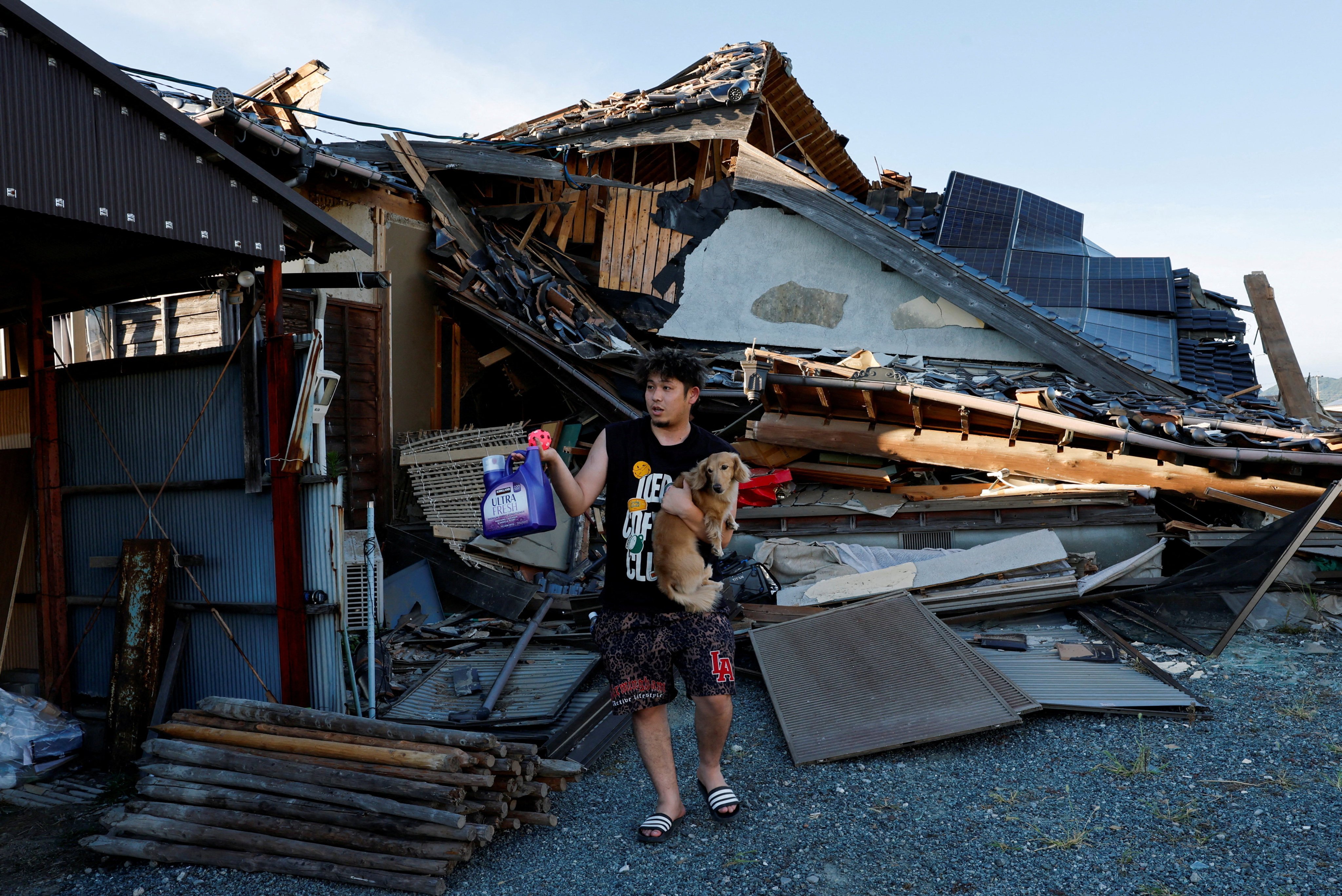 A man holding his pet dog stands in front of a house that collapsed in an earthquake in Japan’s Kumamoto prefecture on July 31. Photo: Reuters