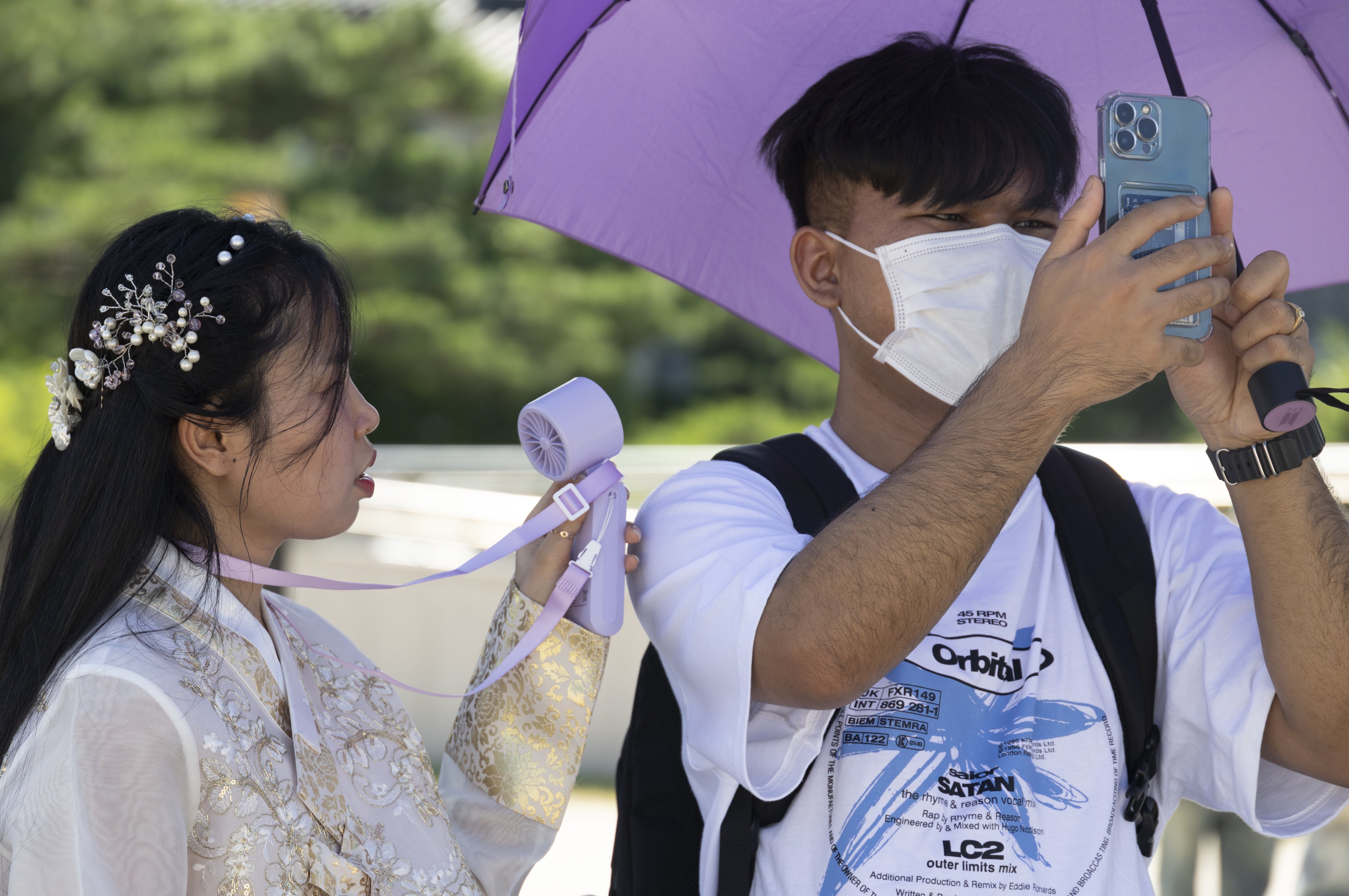 Two tourists use a hand fan and an umbrella to seek relief from the extreme heat in Seoul on Thursday. Photo: EPA