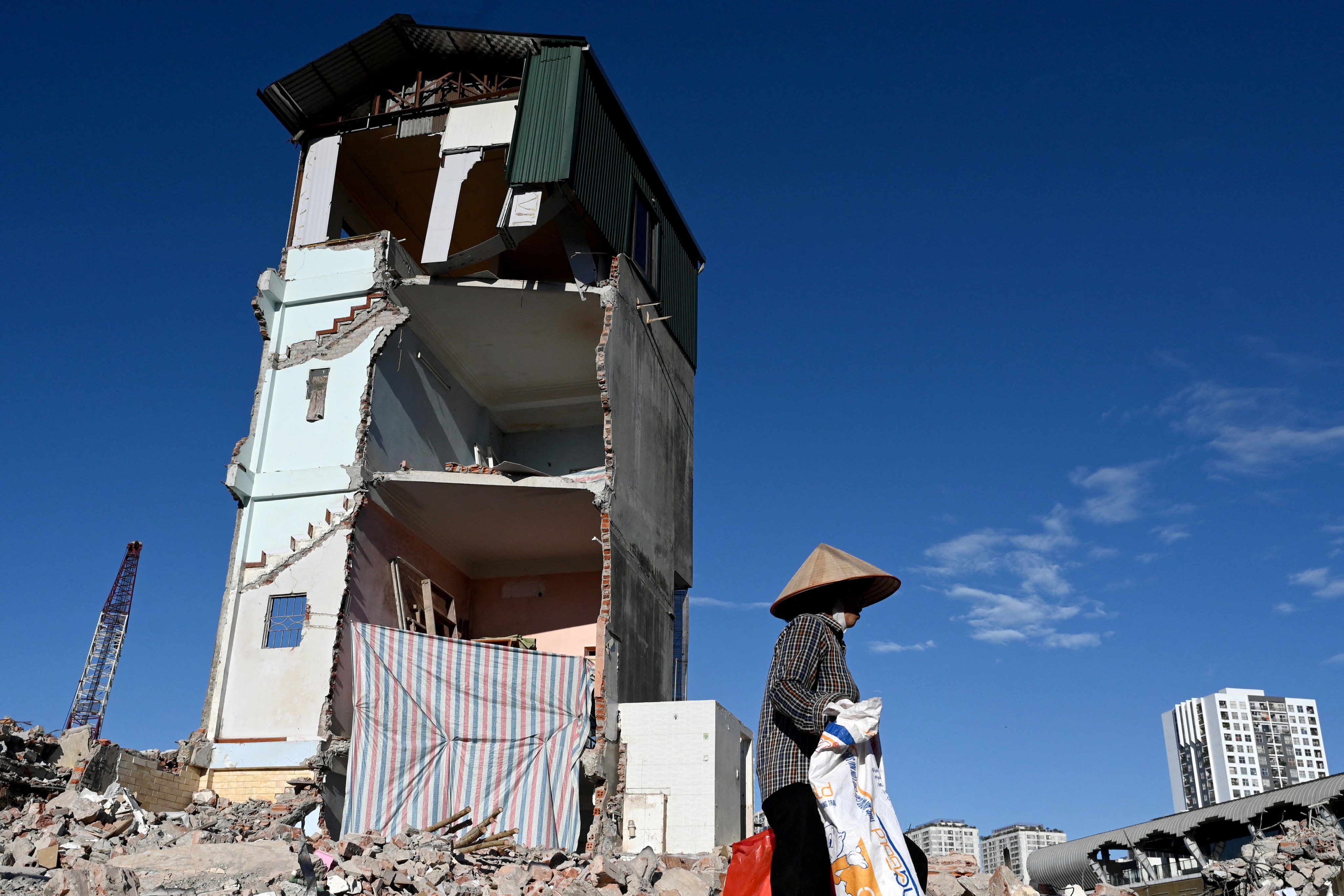 A woman walks past the remnants of a house still standing after demolition to make way for an expanded road network in Hanoi on May 25, 2026. (Photo by Nhac NGUYEN / AFP)