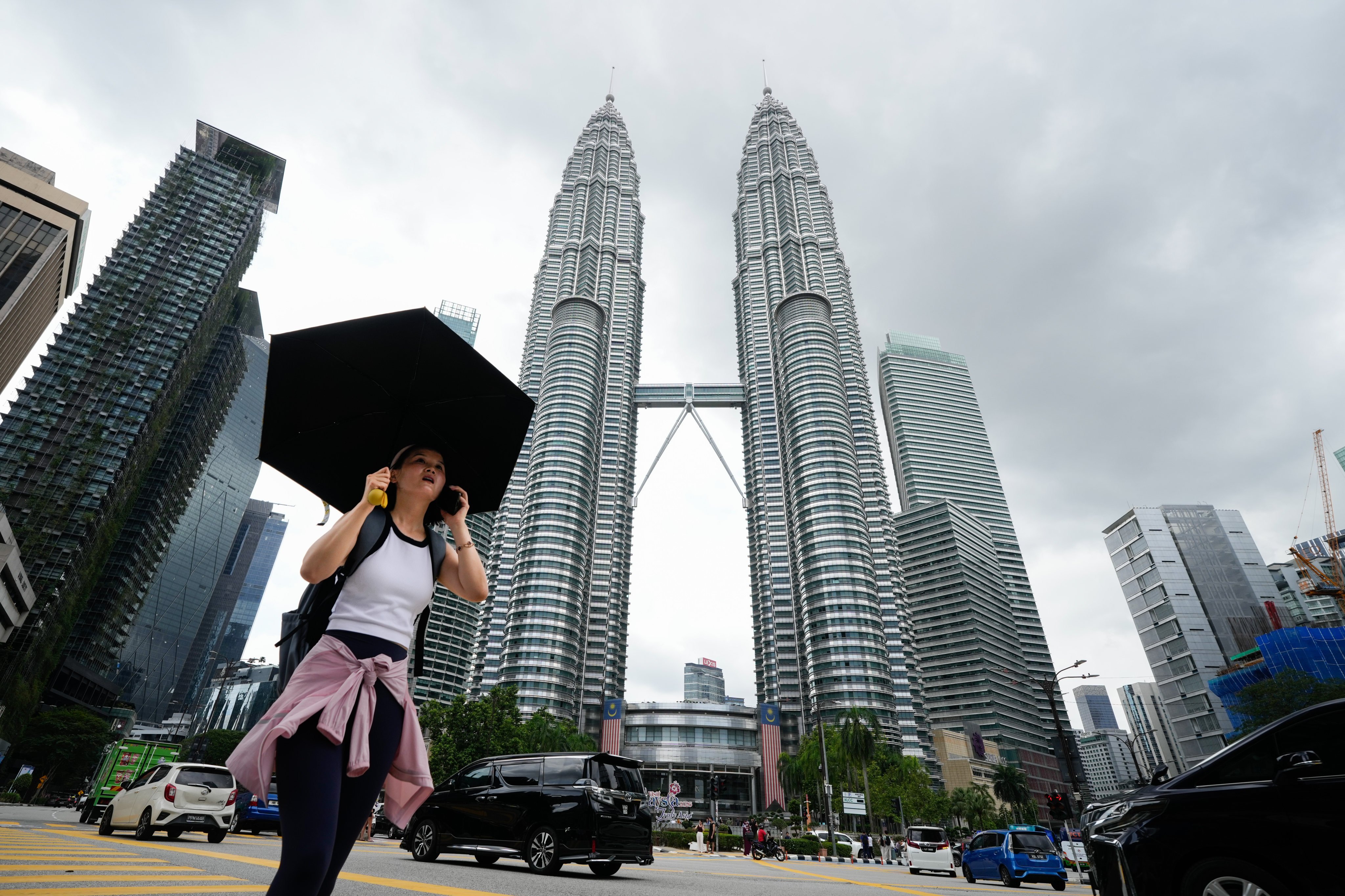 A pedestrian carries an umbrella crosses a street in front of the Petronas Twin Towers in Kuala Lumpur, Malaysia, on Tuesday. Photo: AP