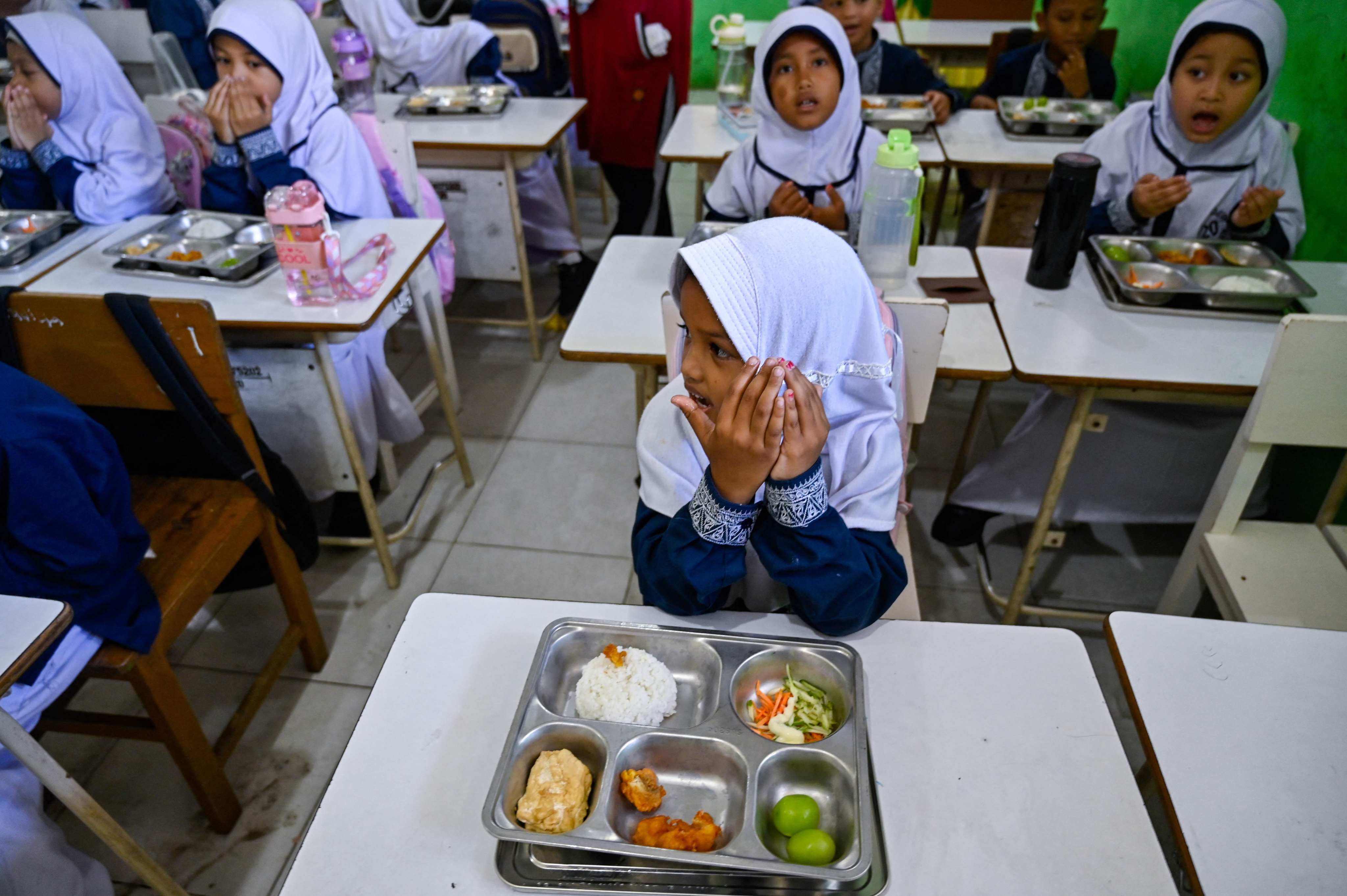Students pray before eating free meals supplied by an Indonesian government programme at an elementary school in Banda Aceh in 2025. Fuel and fertiliser costs may impact child nutrition in Asia, with long-term consequences. Photo: AFP