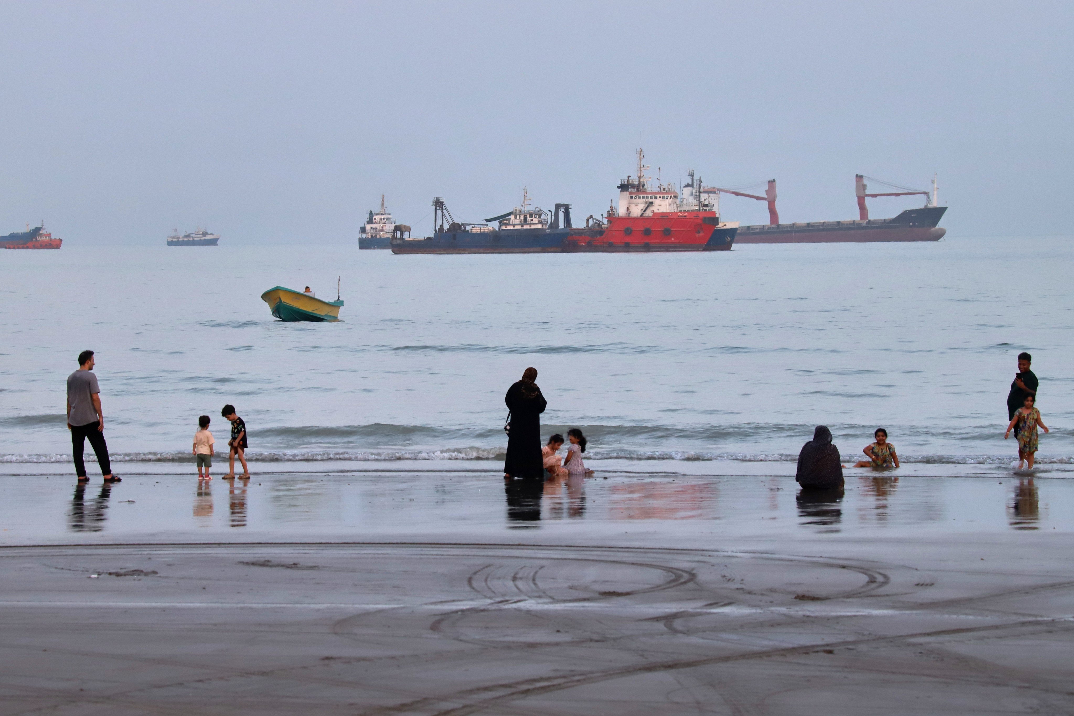 People spend time on a beach as commercial vessels are seen anchored in the Strait of Hormuz off Bandar Abbas, Iran, on Wednesday. Photo: via AP