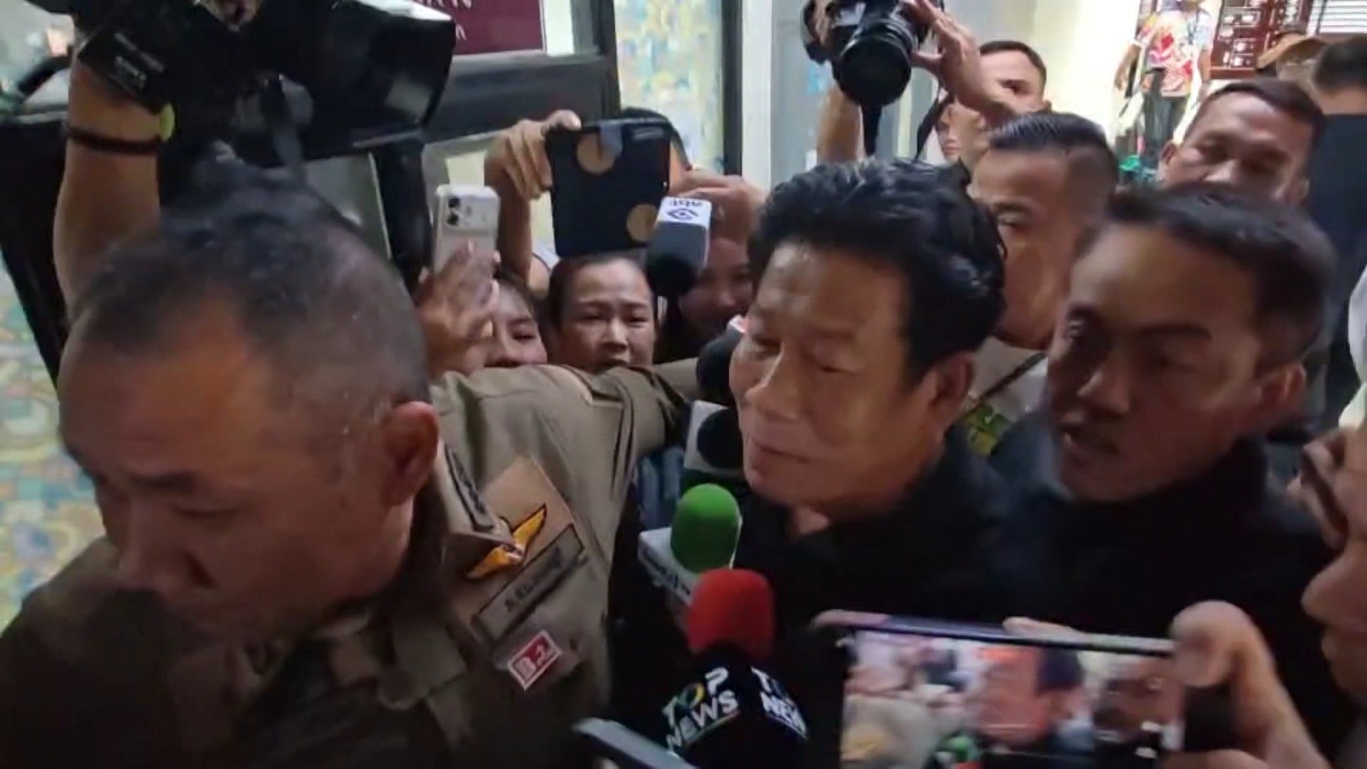 Chalong Riewrang (centre) is escorted by police past members of the media in Nonthaburi on Monday. Photo: TPBS/AP