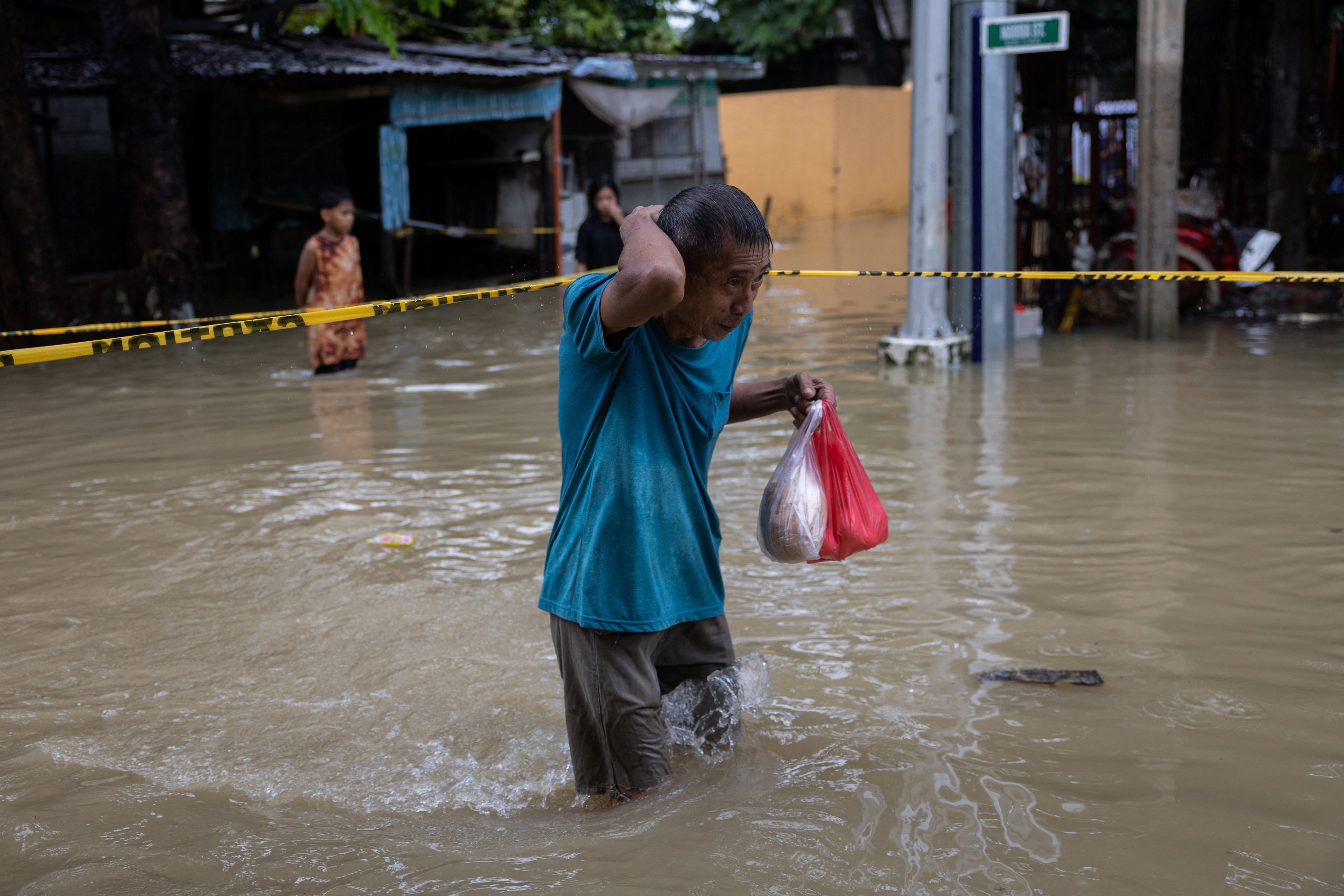A man carrying plastic bags of food wades through floodwater amid southwest monsoon rains in Bagong Silangan, Quezon City, Philippines, August 10, 2026. REUTERS/Eloisa Lopez