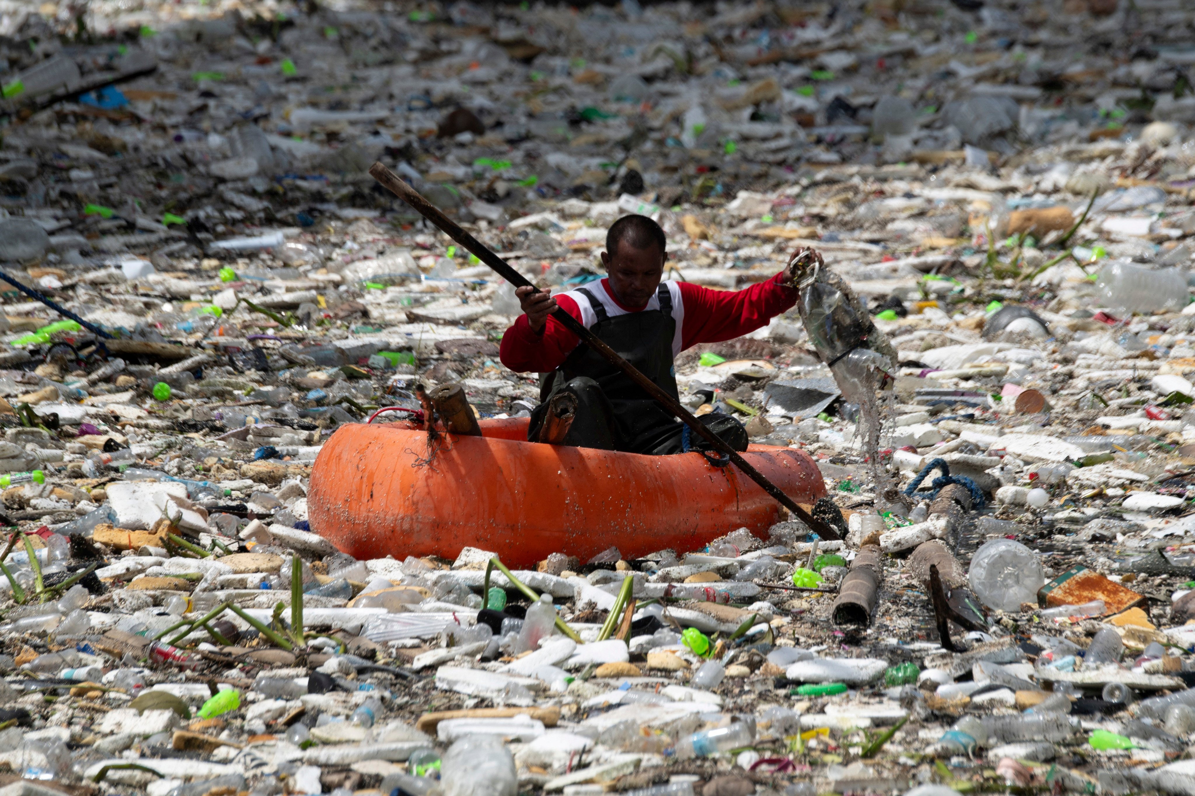 A worker on a plastic boat collects rubbish washed up on a river at the height of heavy rains enhanced by the Southwest monsoon days before, near a shopping complex in Paranaque City, suburban Manila on August 11, 2026. Floods, landslides and accidents driven by a nine-day downpour equivalent to more than a month’s worth of rain in some areas have killed at least 16 people in the northern Philippines, rescuers said on August 10. (Photo by Ted ALJIBE / AFP)