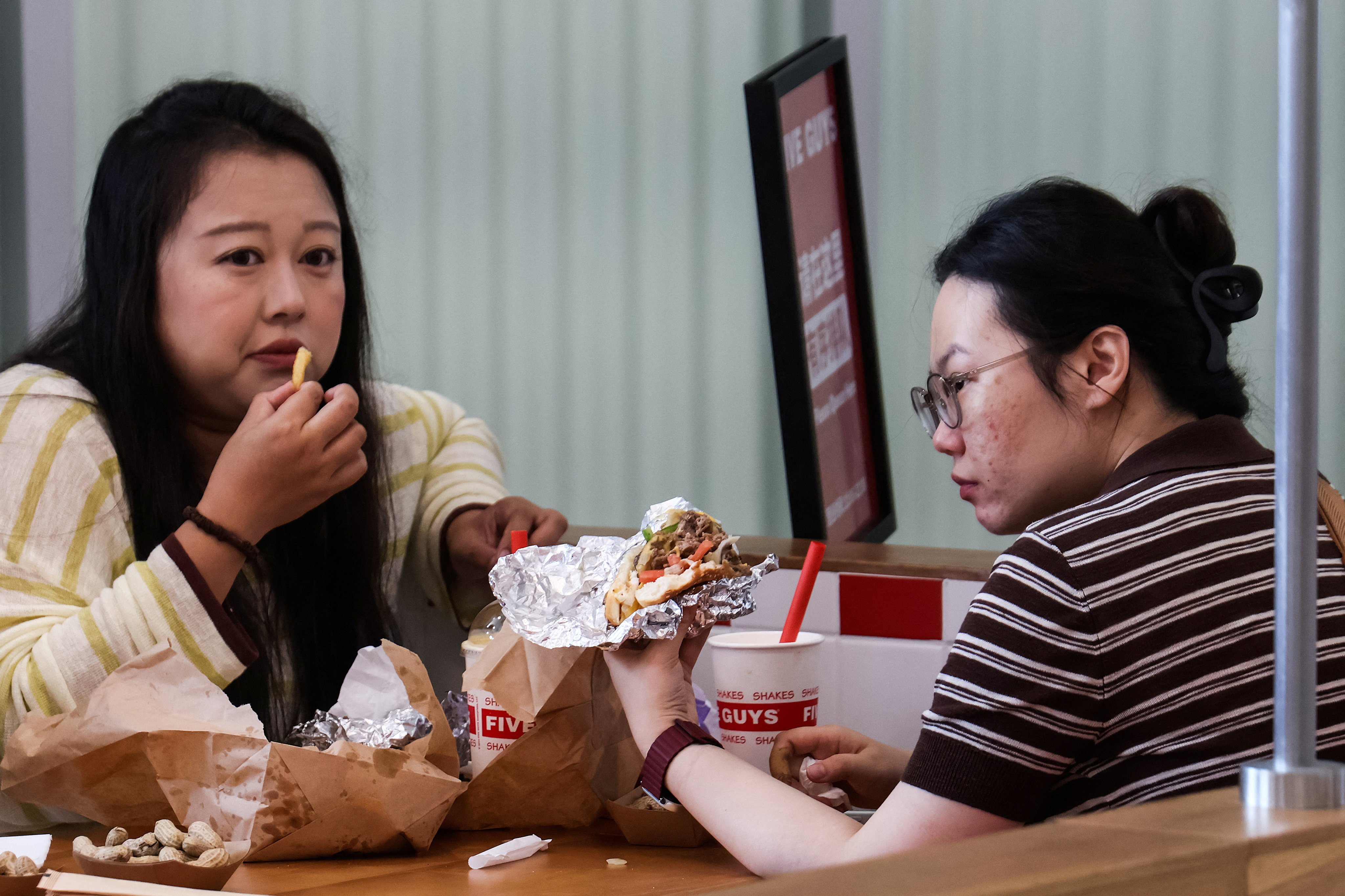 Two women eat at a Five Guys fast-food restaurant after the US burger chain opened its first two locations in Beijing, China, in August 2026. Photo: Reuters